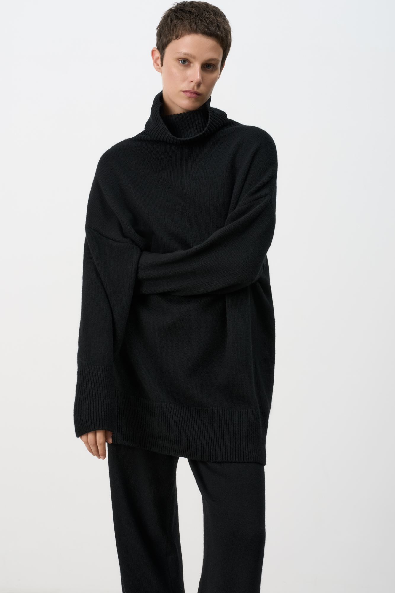 Трикотажный джемпер из мягкой шерсти с добавлением кашемира. Высокий ворот, заниженная линия плеч, удлиненная спинка. Края изделия сделаны в широкий рубчик. Можно дополнить комплектными брюками.