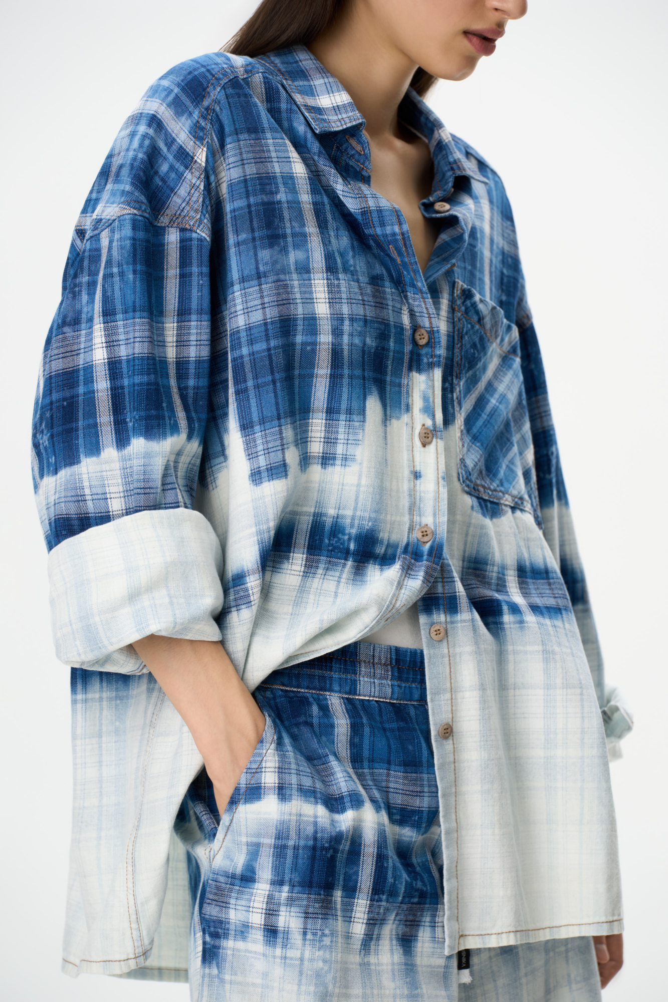 Рубашка в клетку из 100% хлопка с эффектом тай-дай. Модель свободного силуэта, с длинными рукавами, отложным воротником и карманом на груди. Застежка на пуговицы. Дополнить образ можно шортами в таком же стиле.