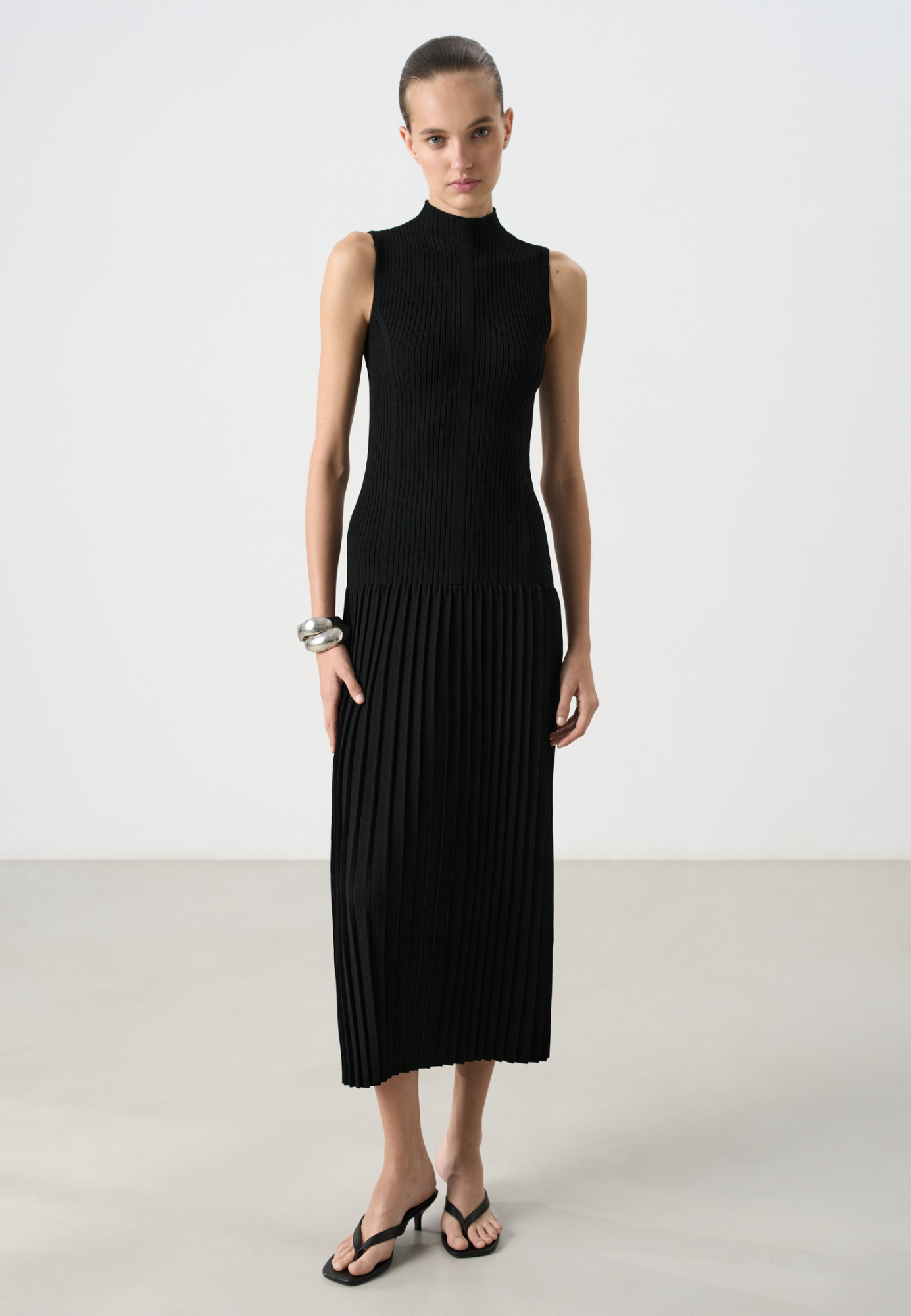 Трикотажное платье длины макси из вискозы. Модель приталенного силуэта, без рукавов, с невысоким воротником-стойкой и юбкой плиссе от бедер.
