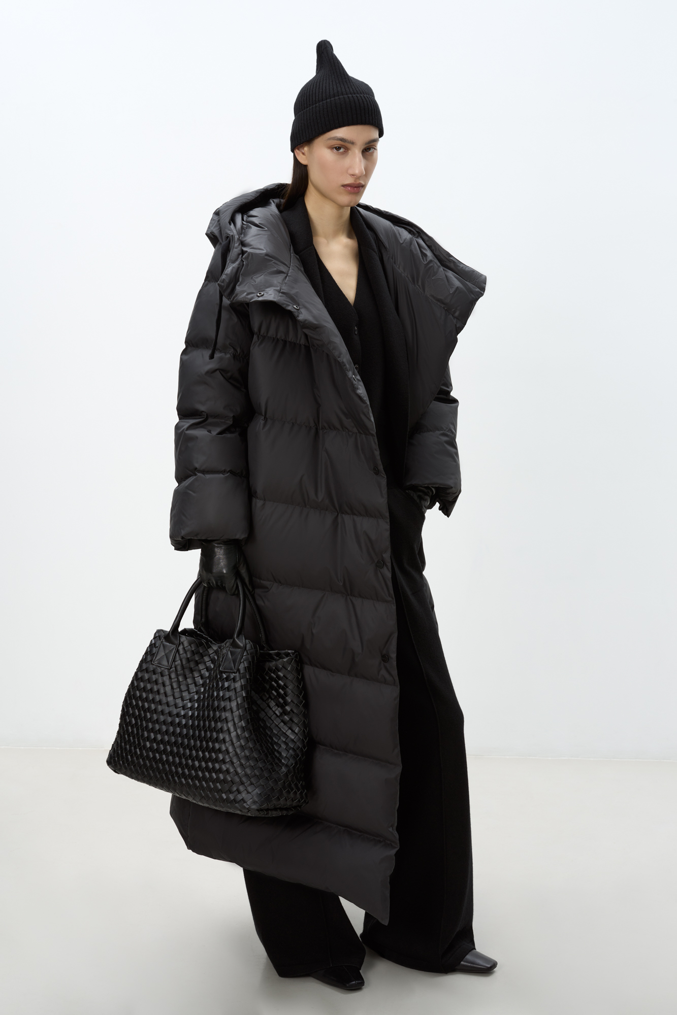 Длинный стеганый пуховик с косой застежкой на кнопки. Модель с ассиметричным низом, боковыми карманами и капюшоном. В комплекте пояс в тон.