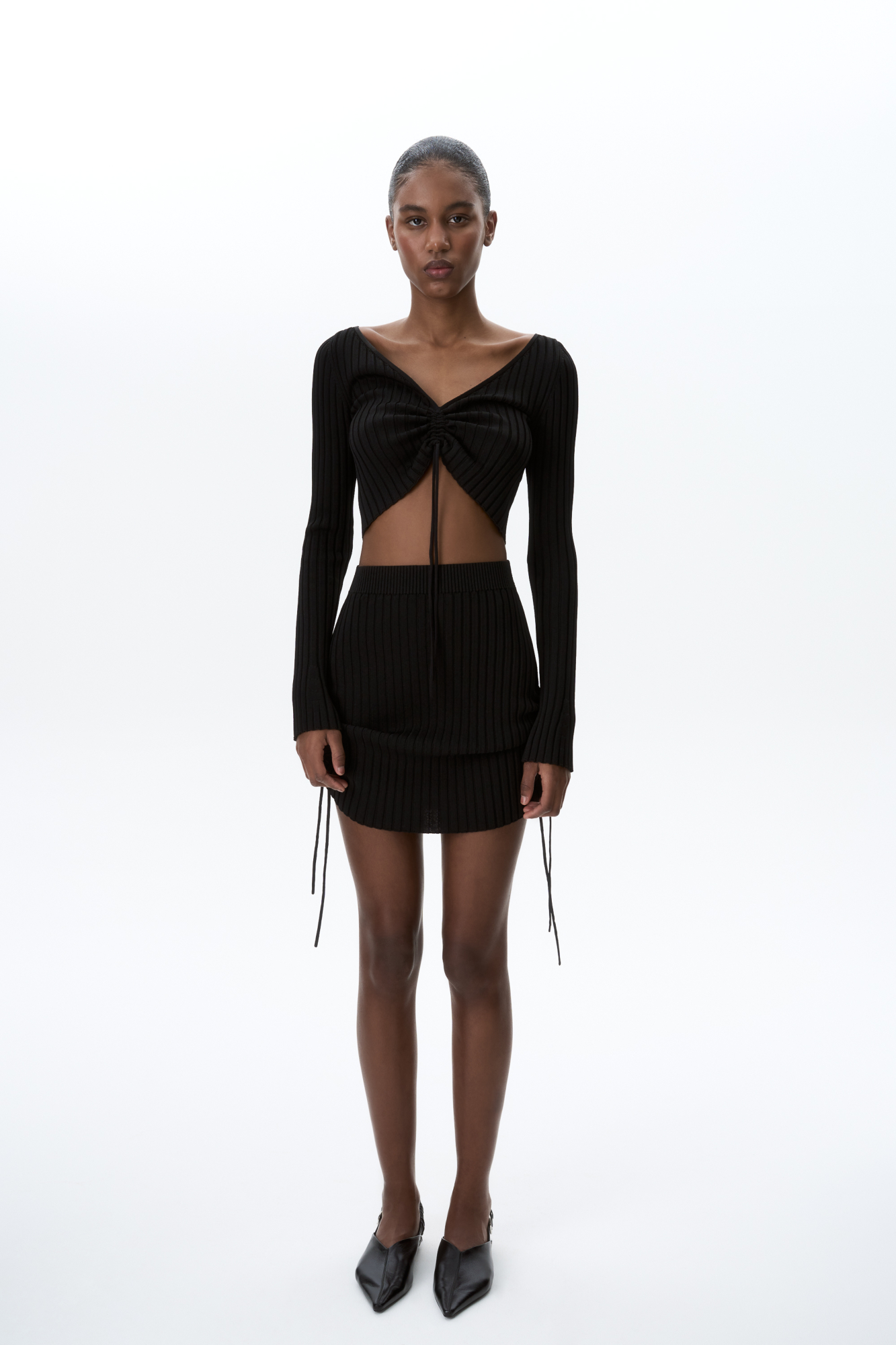 Трикотажная юбка длины мини из вискозы. Модель с драпировкой по бокам, регулируемой кулиской и эластичным поясом на резинке. Дополнить образ можно топом в таком же стиле.