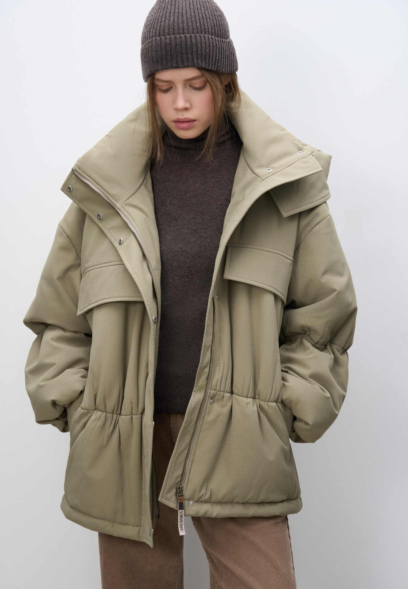 Длинная куртка на синтепоне из текстурной ткани. Модель свободного силуэта со спущенной линией плеча, накладными и боковыми карманами, воротником-стойкой и капюшоном. Изделие на подкладке. Застежка на молнию под планкой с кнопками.