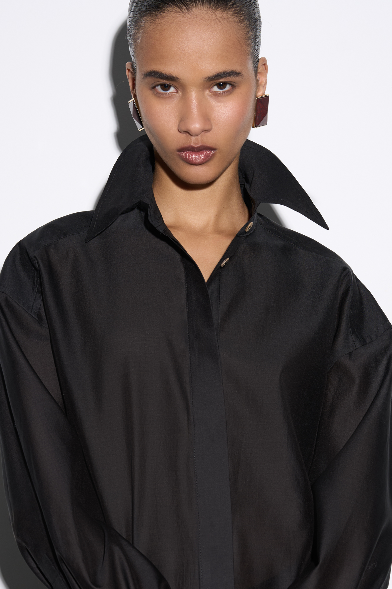 Рубашка из шелка с добавлением хлопка. Модель прямого кроя с длинными рукавами с манжетами, классическим отложным воротником, увеличенными плечами и завязкой на спинке. Застежка на пуговицы под планкой.