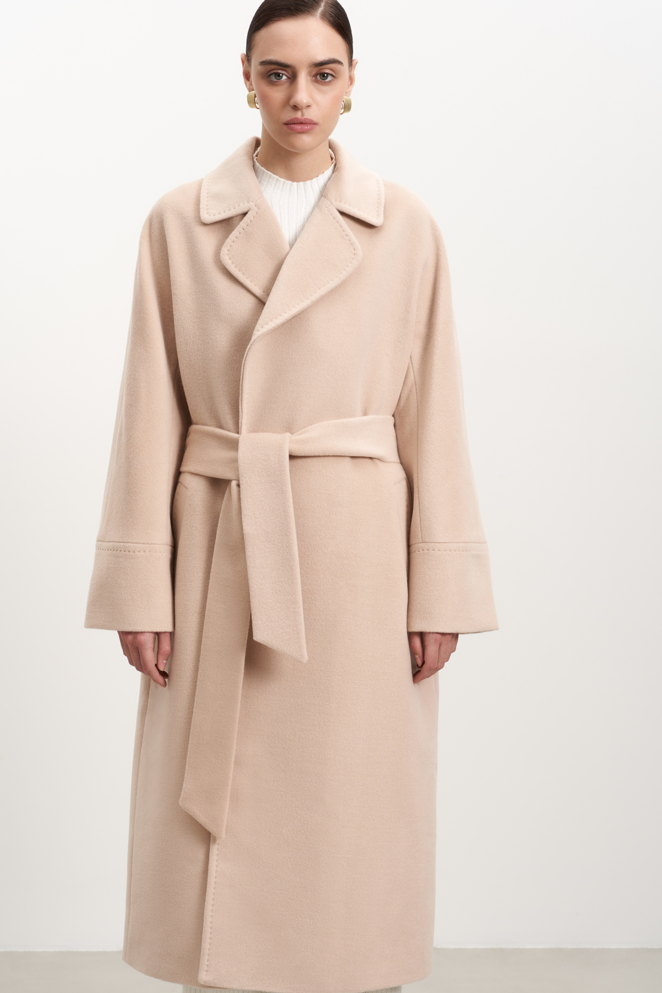 Длинное шерстяное пальто на запах на подкладке без застежки, с поясом из основной ткани. V-образный вырез с лацканами. Два кармана в боковых швах. <br />
