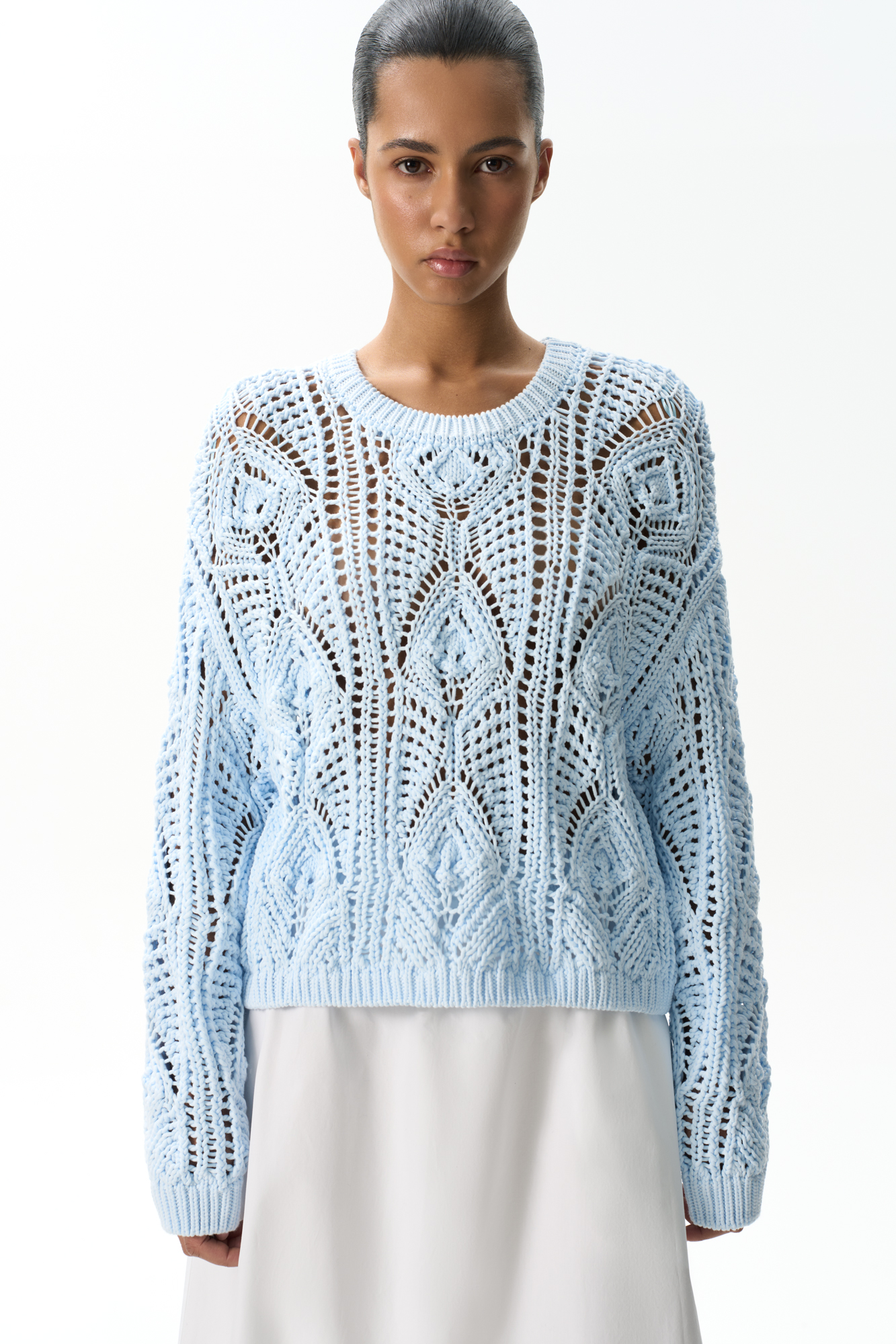 Трикотажный джемпер из хлопка, выполненный ажурной вязкой с орнаментом. Модель свободного силуэта с длинными рукавами и круглым вырезом горловины. Манжеты и низ изделия выполнены в рубчик.