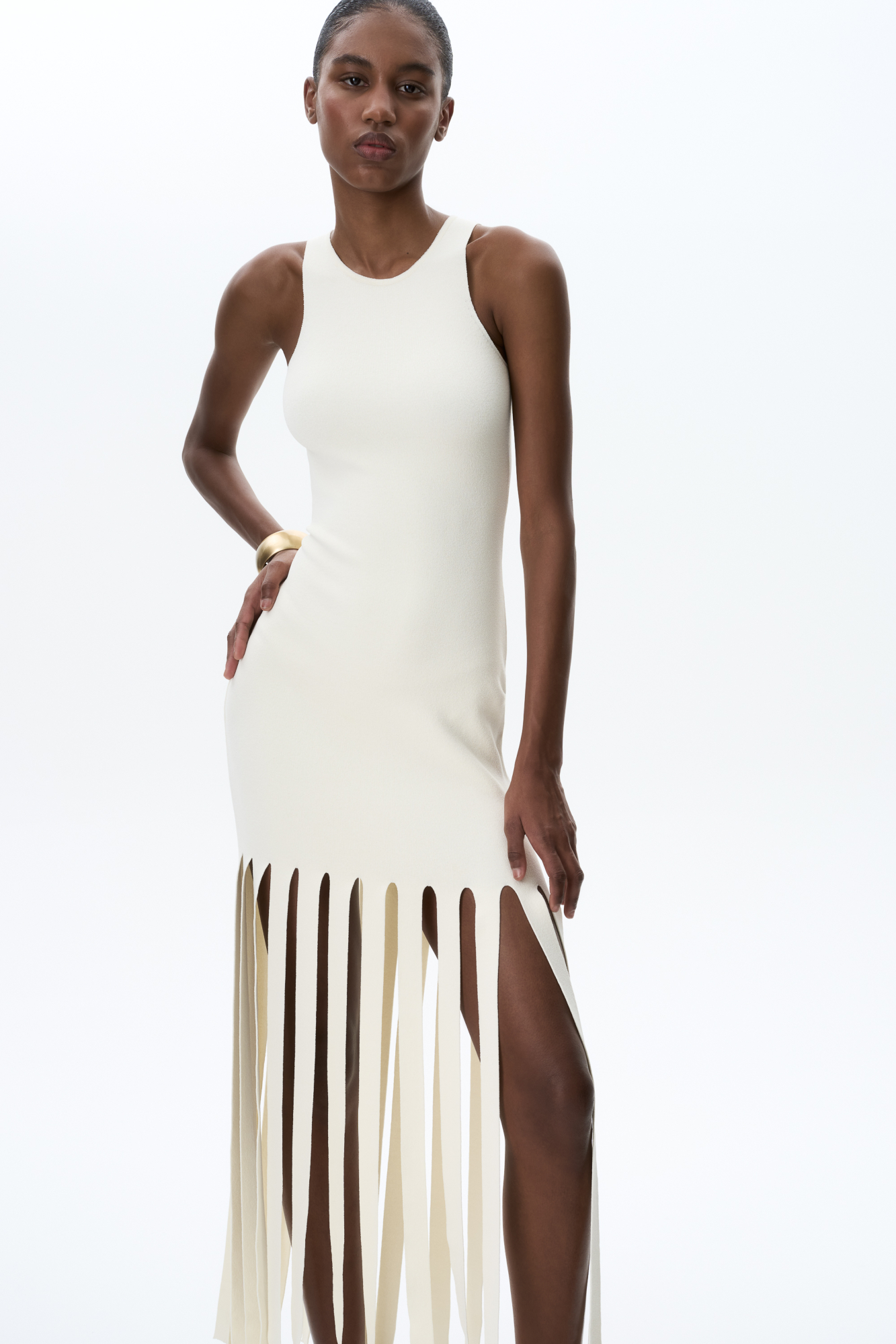 Трикотажное платье длины мини из мягкой вискозы. Модель прителенного лисуэта, без рукавов и круглым вырезом горловины. Изделие декорировано бахромой из широких лент.