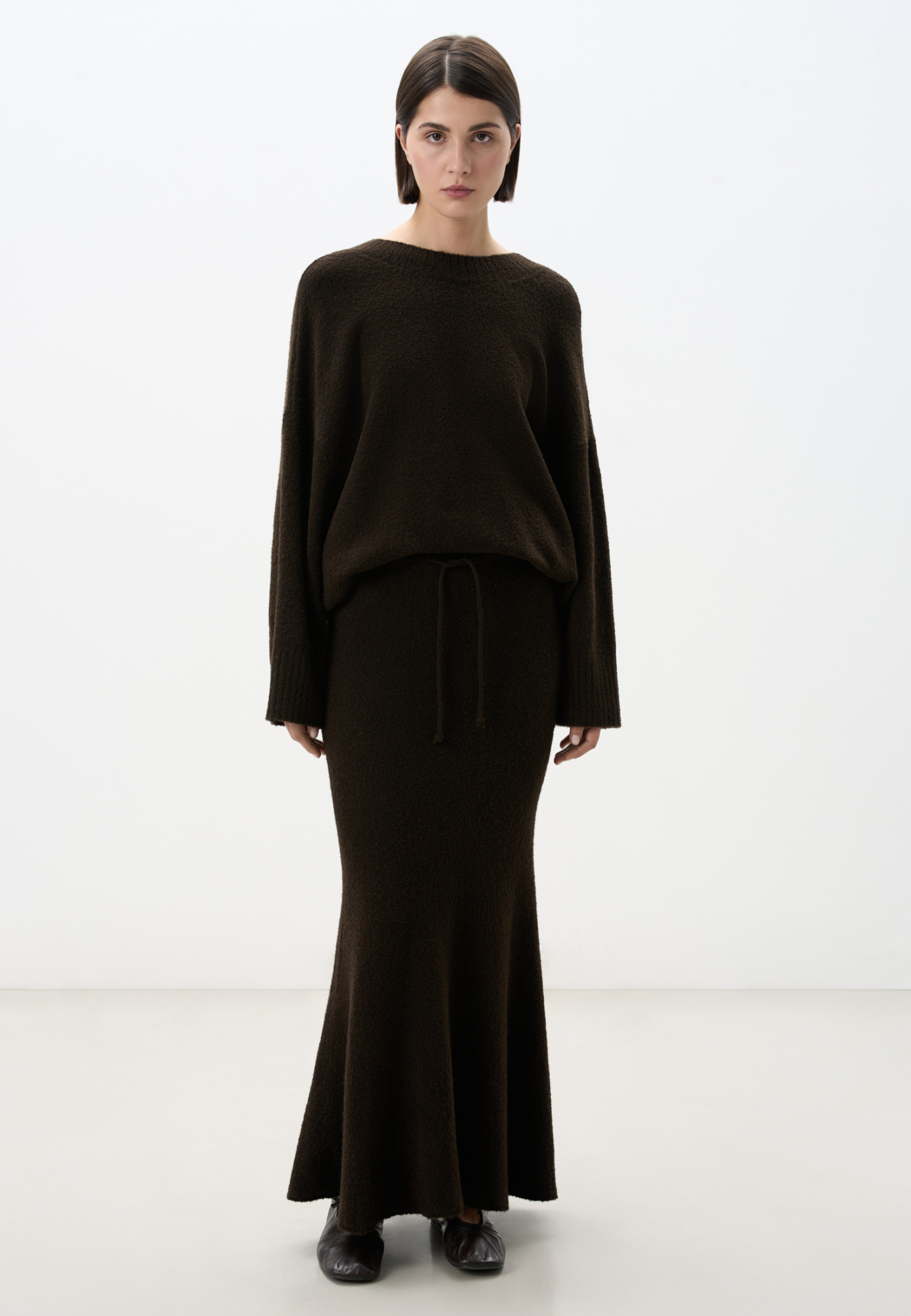 Трикотажная юбка длины макси из буклированной пряжи. Модель по фигуре с расклешенным подолом и поясом, дополненным кулиской. Дополнить образ можно джемпером в таком же стиле. 