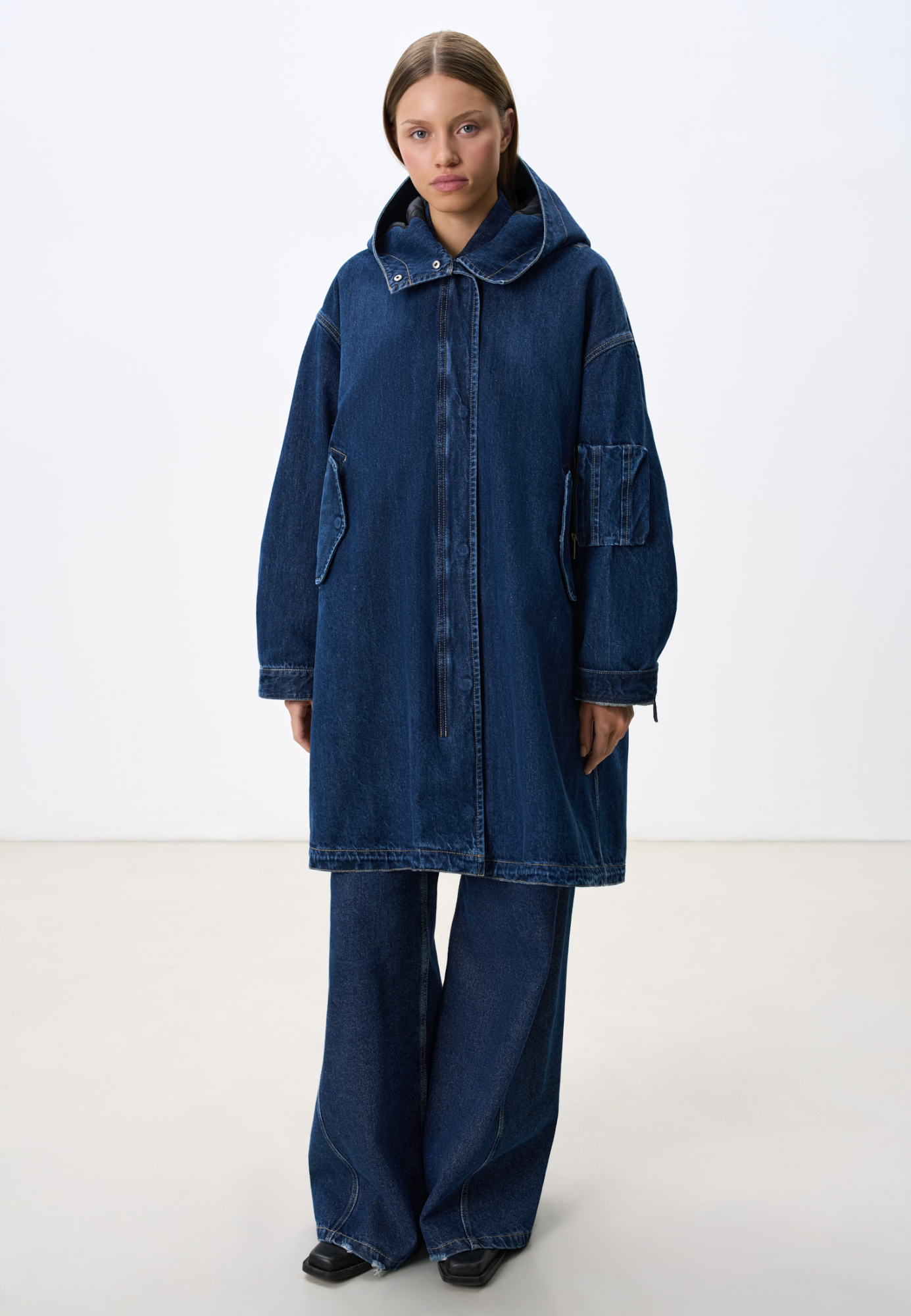 Джинсовая парка из 100% хлопка на стеганой подстежке. Модель свободного кроя, со спущенной линией плеч, глубоким капюшоном, боковыми карманами с клапанами на пуговицах и карманом на рукаве. Застежка на металлические кнопки под планкой. Подстежка отстегивается и может являться отдельным элементом образа.