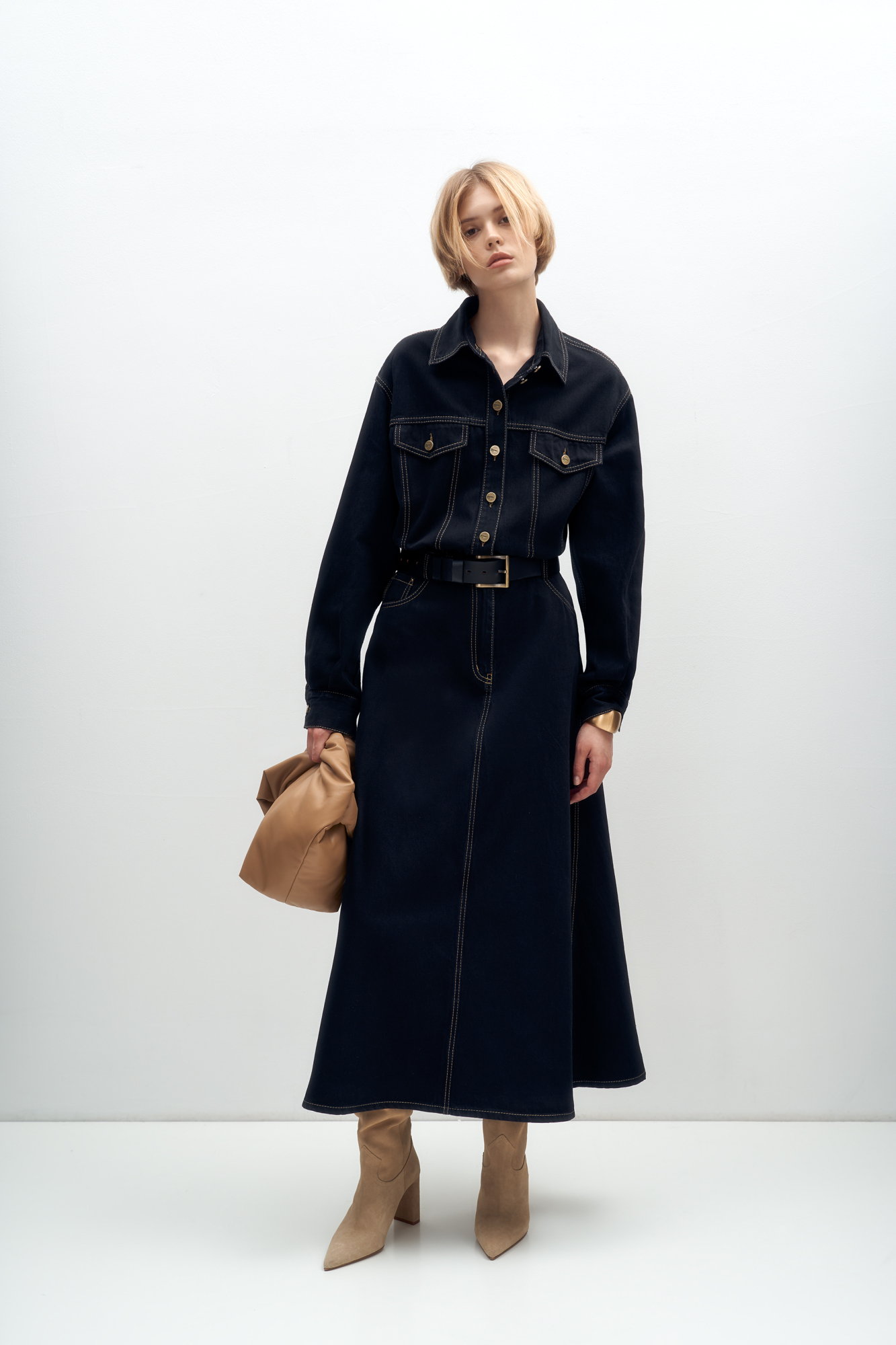 Джинсовое платье из 100% хлопка с рубашечнымм верхом и юбкой А-силуэта. Модель с длинными рукавами с манжетами, отложным воротником, карманами на груди с клапанами, шлевками на поясе для ремня, боковыми и задними карманами. Застежка на металлические пуговицы. Изделие декорировано вытачками контрастного цвета.