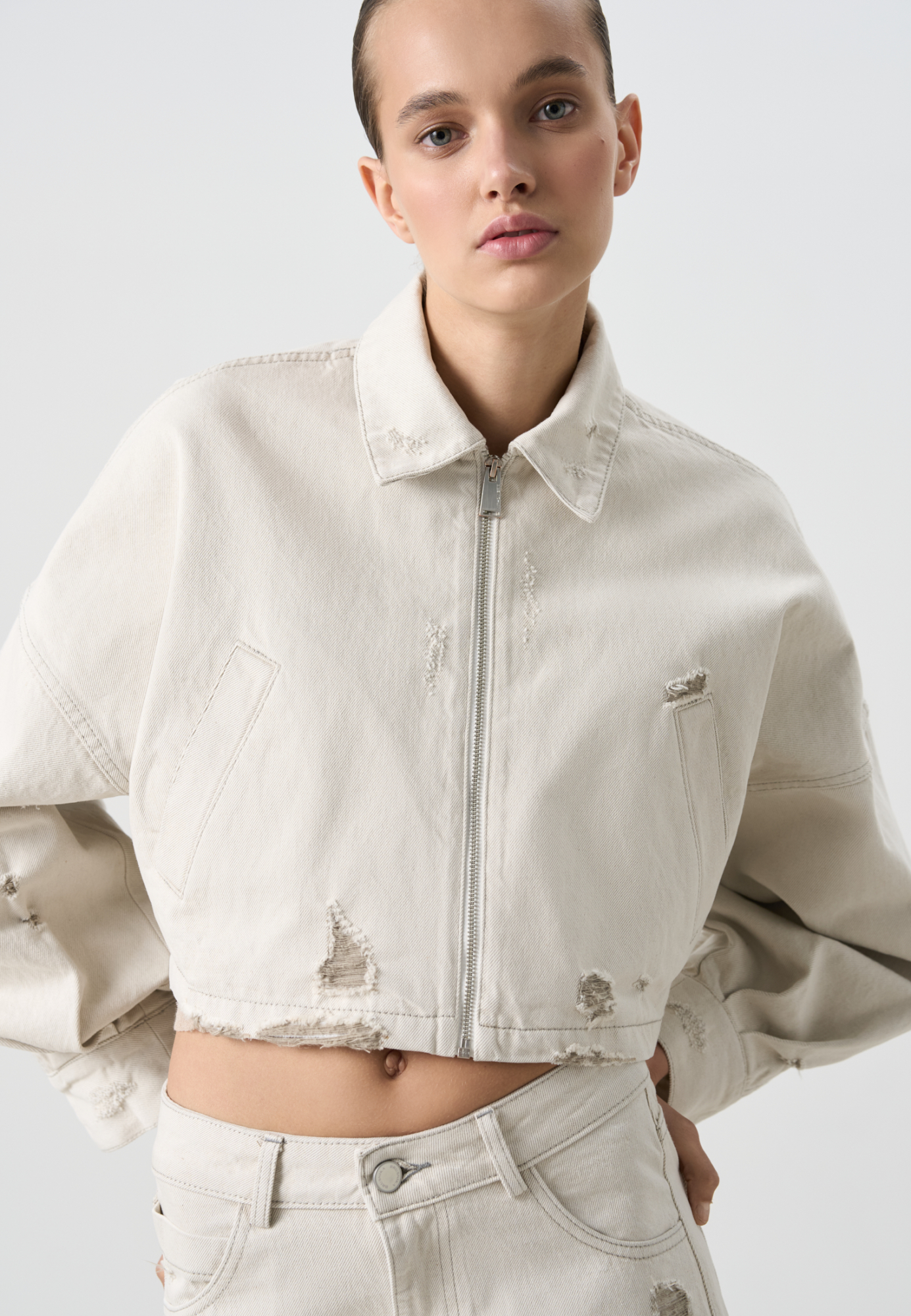 Джинсовая куртка из 100% хлопка. Модель укороченного силуэта с отложным воротником, длинными рукавами, разрезами и эффектом потертости. Застежка на молнию. Дополнить образ можно джинсами в том же стиле. 