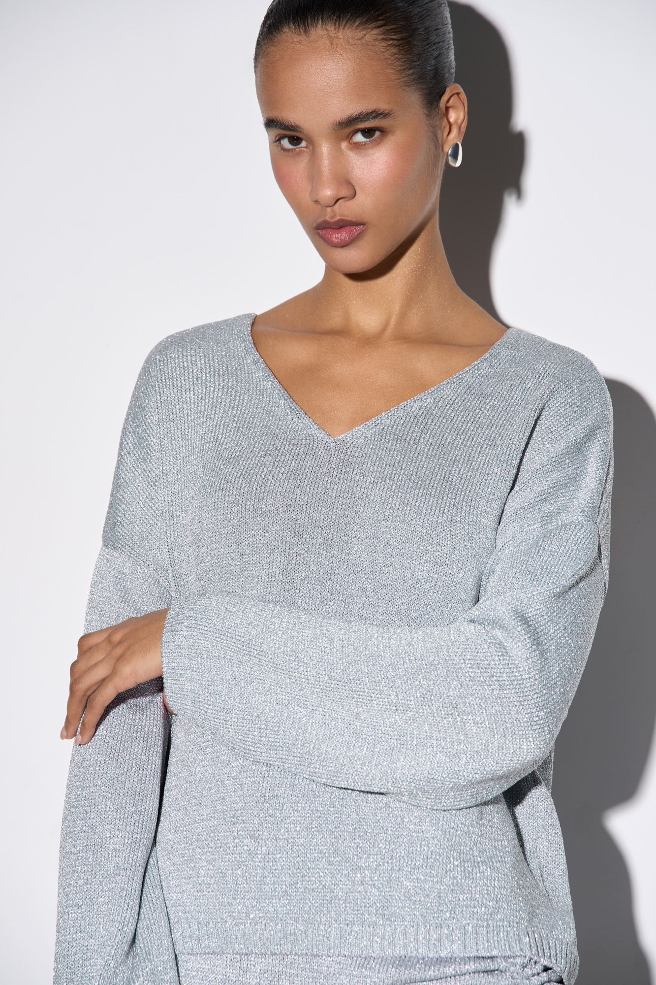 Джемпер из вискозы с добавлением люрекса. Модель свободного силуэта, со спущенной линией плеч и V-образным вырезом. Манжеты рукавов и низ изделия выполнены в рубчик.