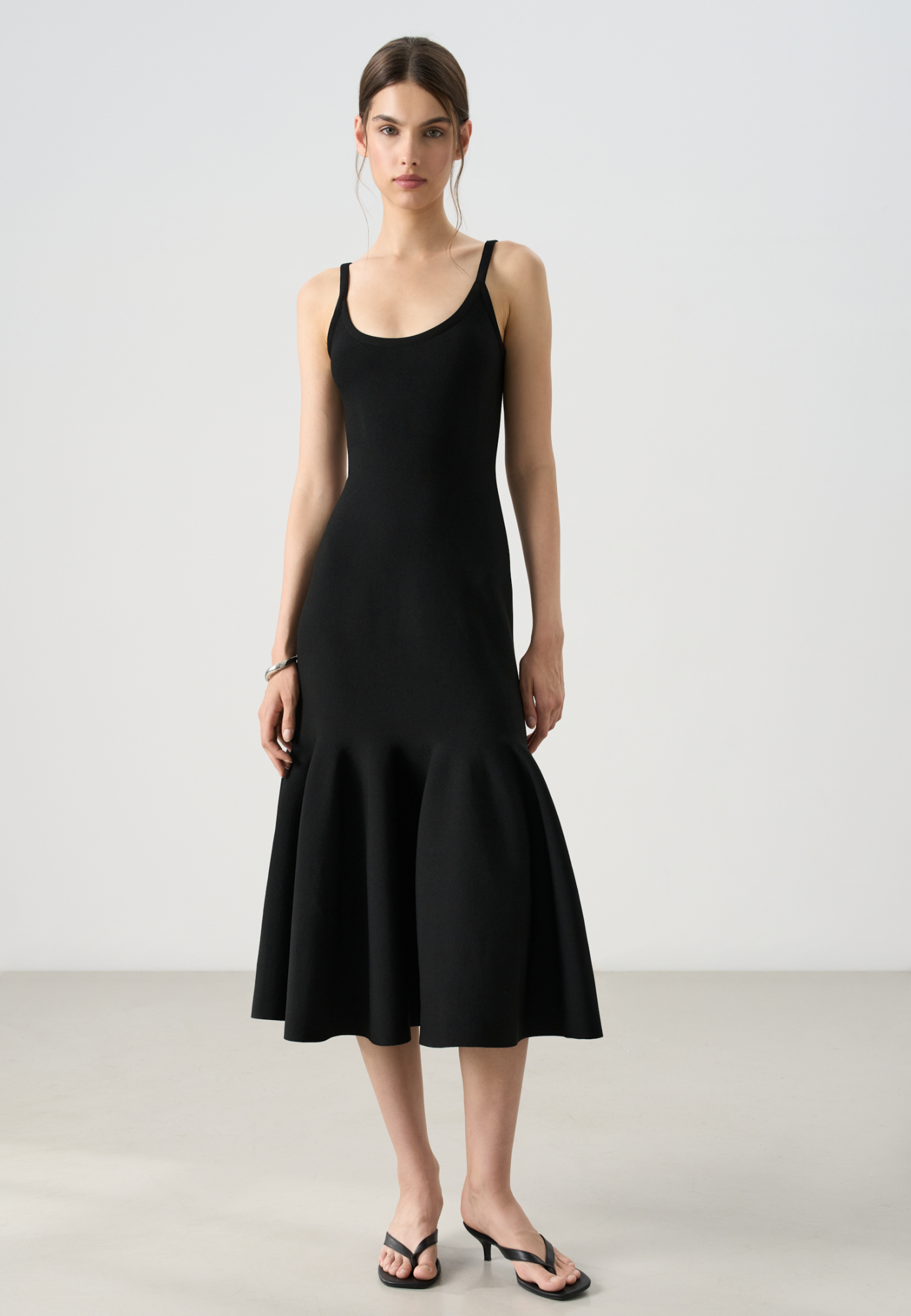 Трикотажное платье длины миди из вискозы. Модель приталенного силуэта, с расклешенной юбкой с мягкими складками, без рукавов, на узких бретелях. Застежка на молнию сзади.