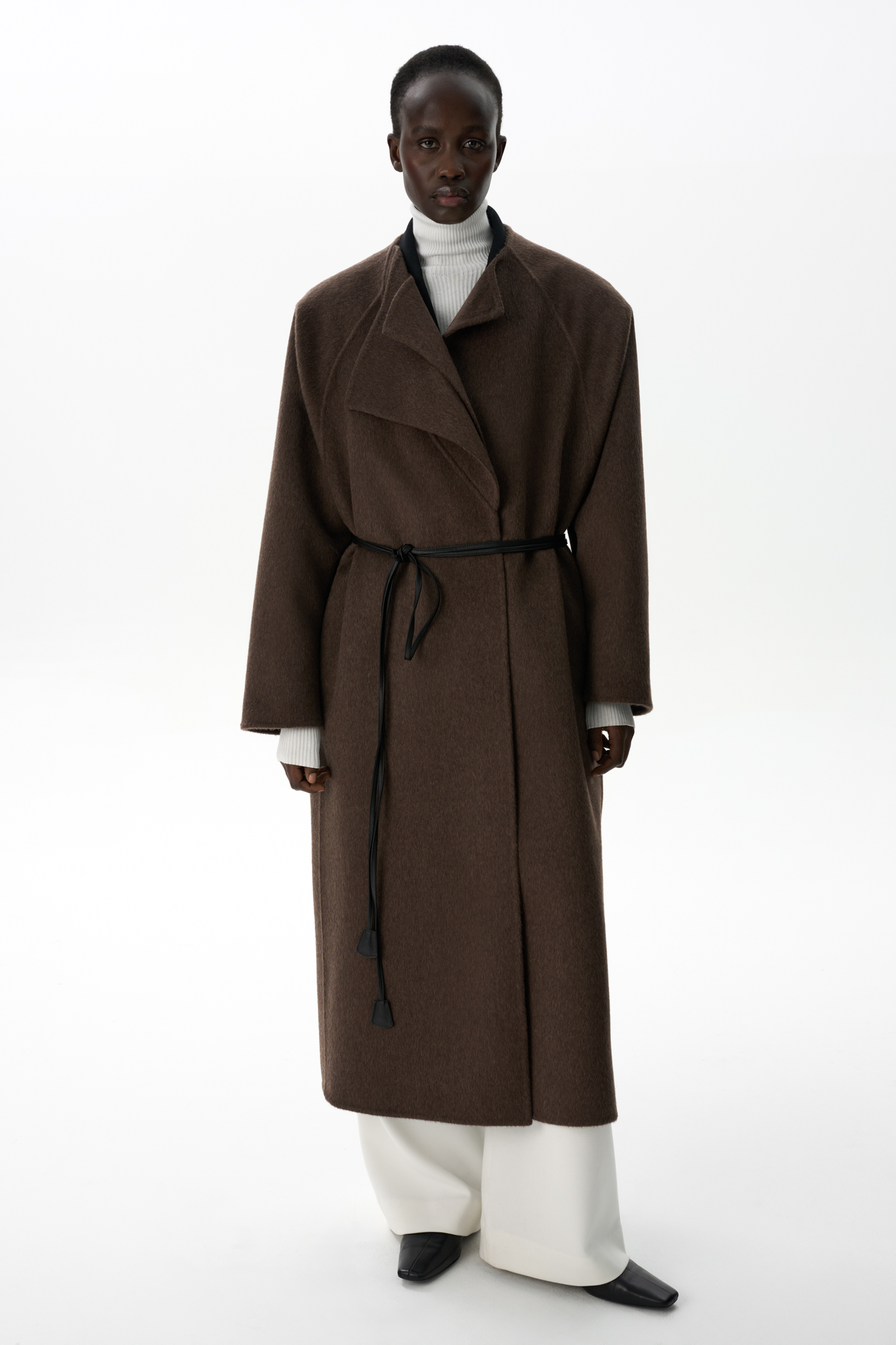 Шерстяное пальто из двусторонней ткани. Модель прямого кроя без воротника. Застежка на скрытые магнитные пуговицы. Изделие без подкладки. Модель декорирована асимметричным лацканом. Пояс из экокожи в комплекте.