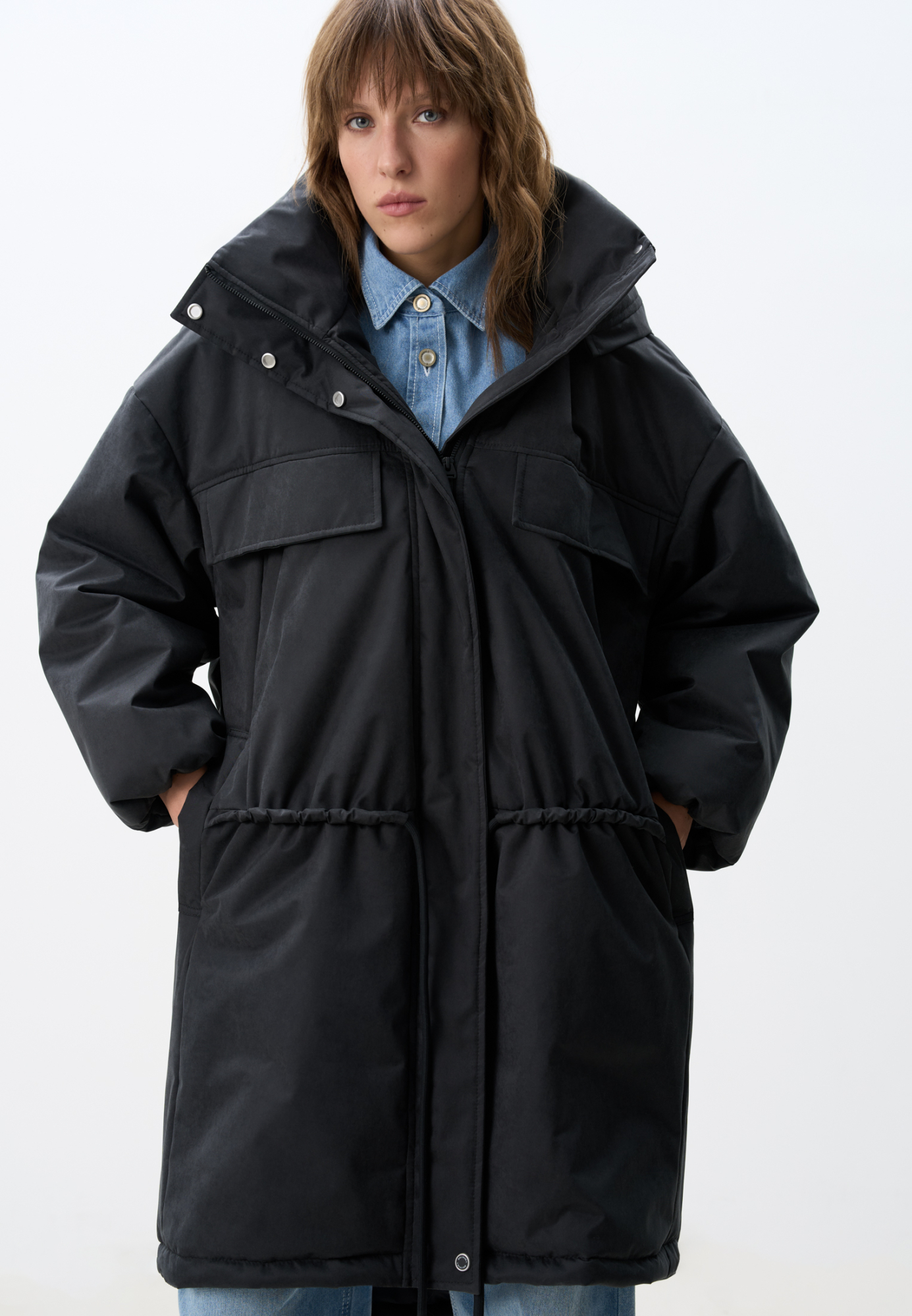 Длинная куртка на синтепоне с капюшоном. Модель свободного силуэта со спущенной линией плеча, накладными и боковыми карманами, регулируемой кулиской на поясе. Изделие на подкладке. Застежка на молнию и магнитные кнопки.