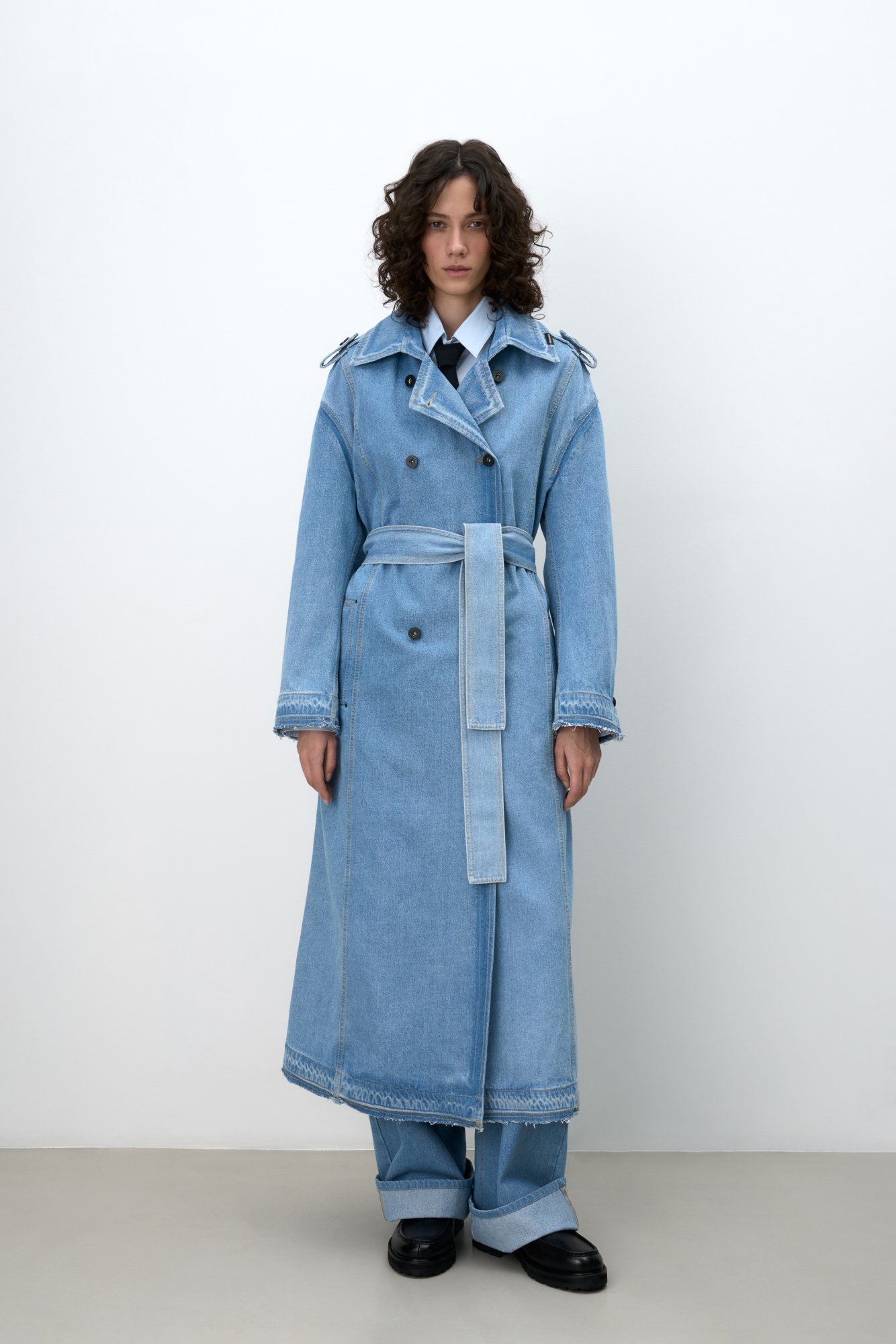 Двубортный джинсовый oversize тренч на запах без подкладки с необработанными краями. Асимметричная отлетная кокетка, отложной воротник, паты на манжетах и широкий пояс из основного материала. Передние боковые карманы на пуговицах.