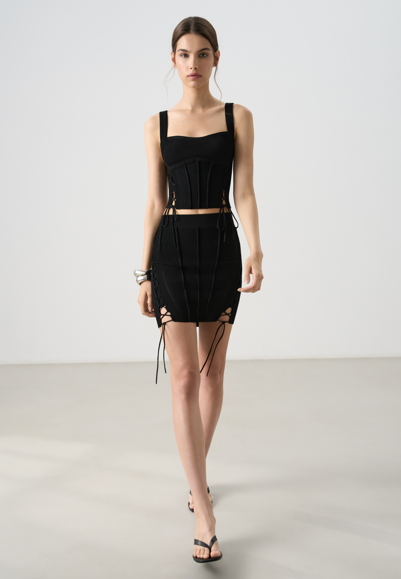 Трикотажная юбка-карандаш длины мини из вискозы. Модель по фигуре, с широким эластичным поясом в рубчик, вертикальными объемными валиками и высокими симметричными разрезами со шнуровкой. Дополнить образ можно топом в таком же стиле.