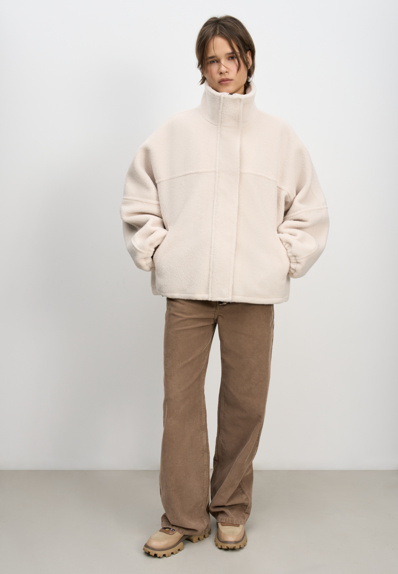 Шуба из экомеха с воротником-стойкой. Модель свободного силуэта с боковыми карманами, объемными швами и манжетами на резинке. Застежка на молнию под планкой с кнопками, декорированной экокожей.