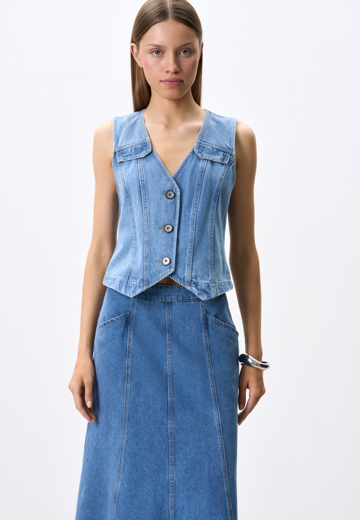 Джинсовый жилет из 100% хлопка. Модель прямого кроя с V-образным вырезом горловины и объемными вертикальными швами. Застежка на три металлические кнопки. Изделие без подкладки.