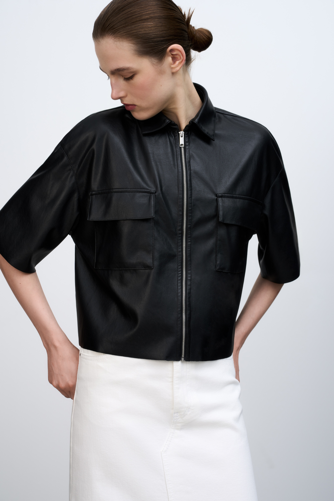 Укороченная рубашка из экокожи. Модель свободного силуэта со спущенной линией плеча, накладными карманами на груди и застежкой на молнию.