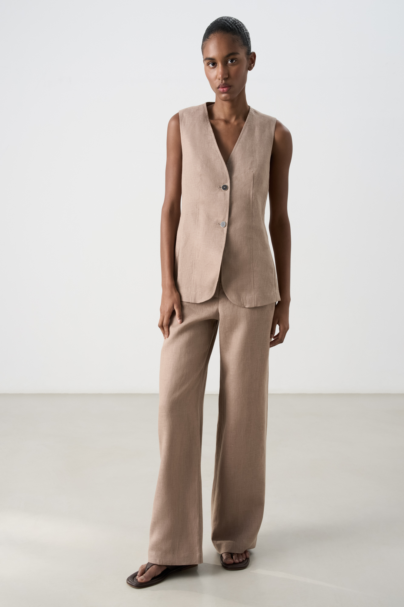 Удлиненный жилет из 100% льна. Модель приталенного силуэта, с V-образным вырезом горловины, вертикальными вытачками, ремнем на спинке и разрезами по бокам. Изделие бех подкладки. 
