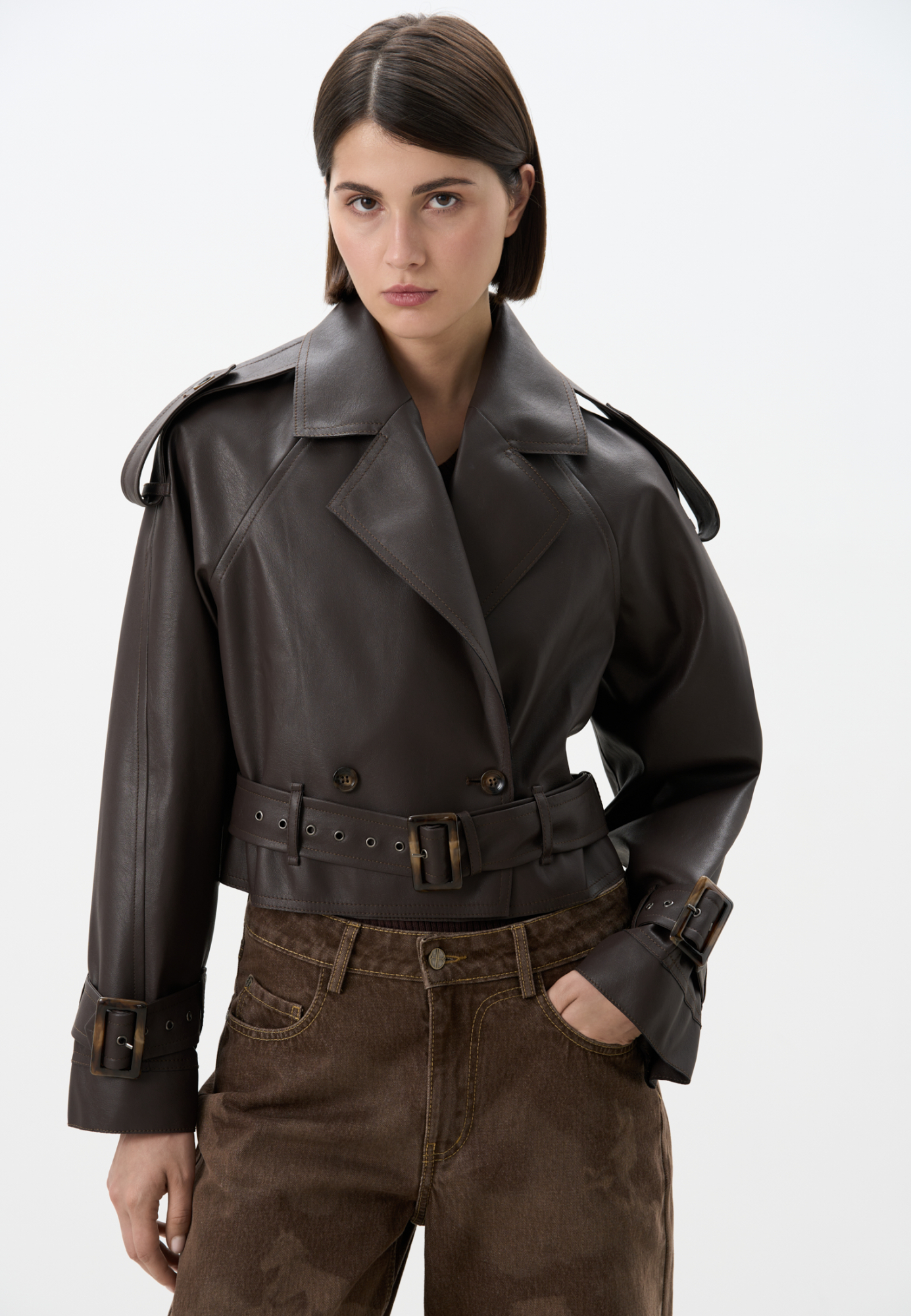 Двубортный жакет-косуха из двусторонней экокожи. Модель свободного силуэта со спущенным плечом и широкими лацканами. Изделие декорировано патами на плечах и ремнями с крупными пряжками на поясе и рукавах. 