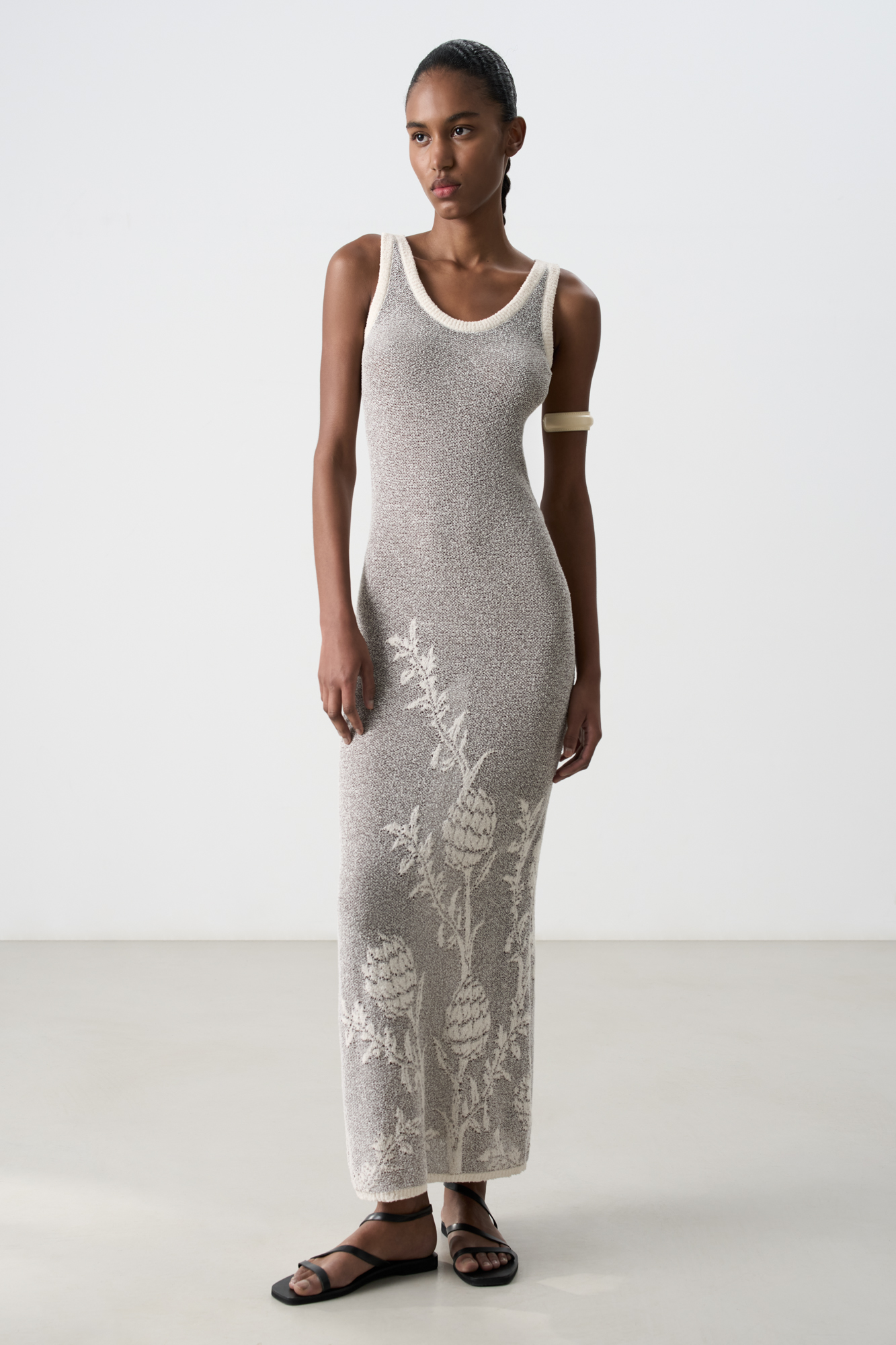 Трикотажное платье длины макси из 100% хлопка. Модель прямого кроя, без рукавов, на тонких бретелях и глубоким вырезом. Изделие декорировано объемным растительным орнаментом. Края выполнены в рубчик.