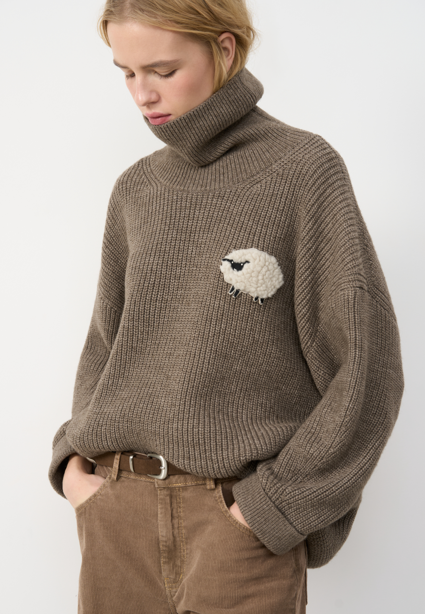 Трикотажный джемпер из шерсти альпака. Модель свободного силуэта, с высоким вывязанным горлом, спущенной линией плеч и длинными рукавами с манжетами. Изделие декорировано объемным элементом в виде барашка.