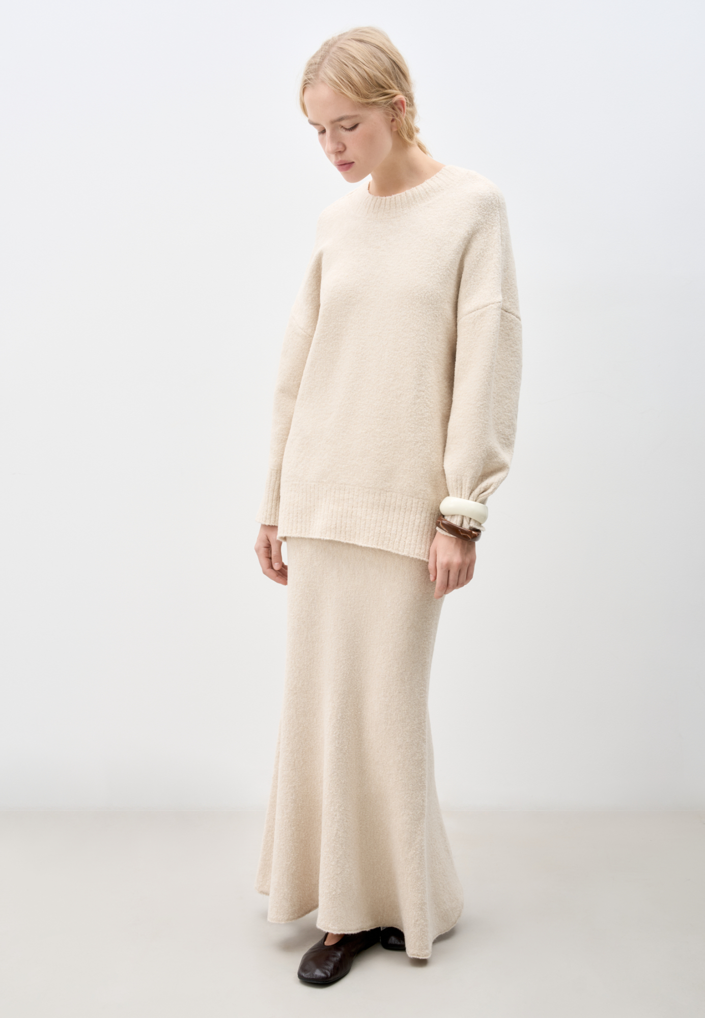 Трикотажная юбка длины макси из буклированной пряжи. Модель по фигуре с расклешенным подолом и поясом, дополненным кулиской. Дополнить образ можно джемпером в таком же стиле. 