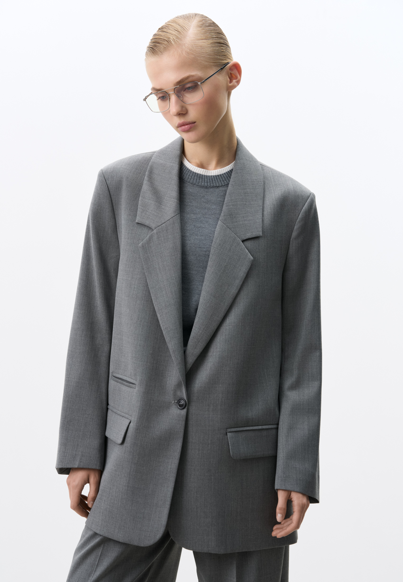 Классический жакет с накладными карманами, подплечниками, разрезами по бокам и удлиненной спинкой. Длинные рукава на манжетах без пуговиц. Застежка на пуговицу.