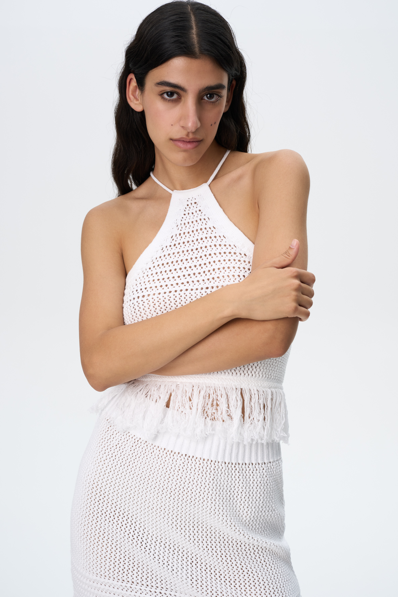 Трикотажный ажурный топ из 100% хлопка. Модель без рукавов, с открытой линией плеч, на тонких бретелях и шнуровкой на спине. Изделие декорировано бахромой по нижнему краю.