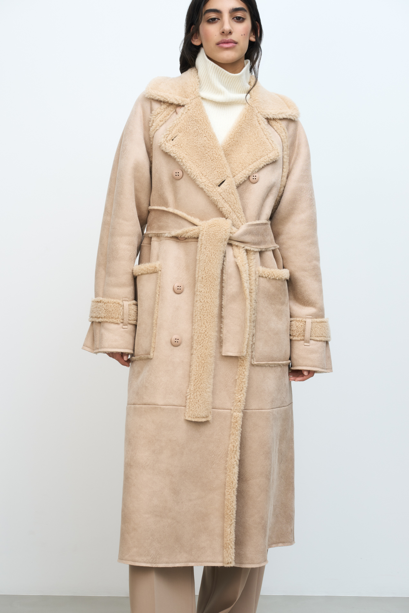 Длинная дубленка из шерсти. Модель прямого силуэта с отложным воротником, накладными карманами, патами и поясом из основного материала. Застежка на пуговицы.