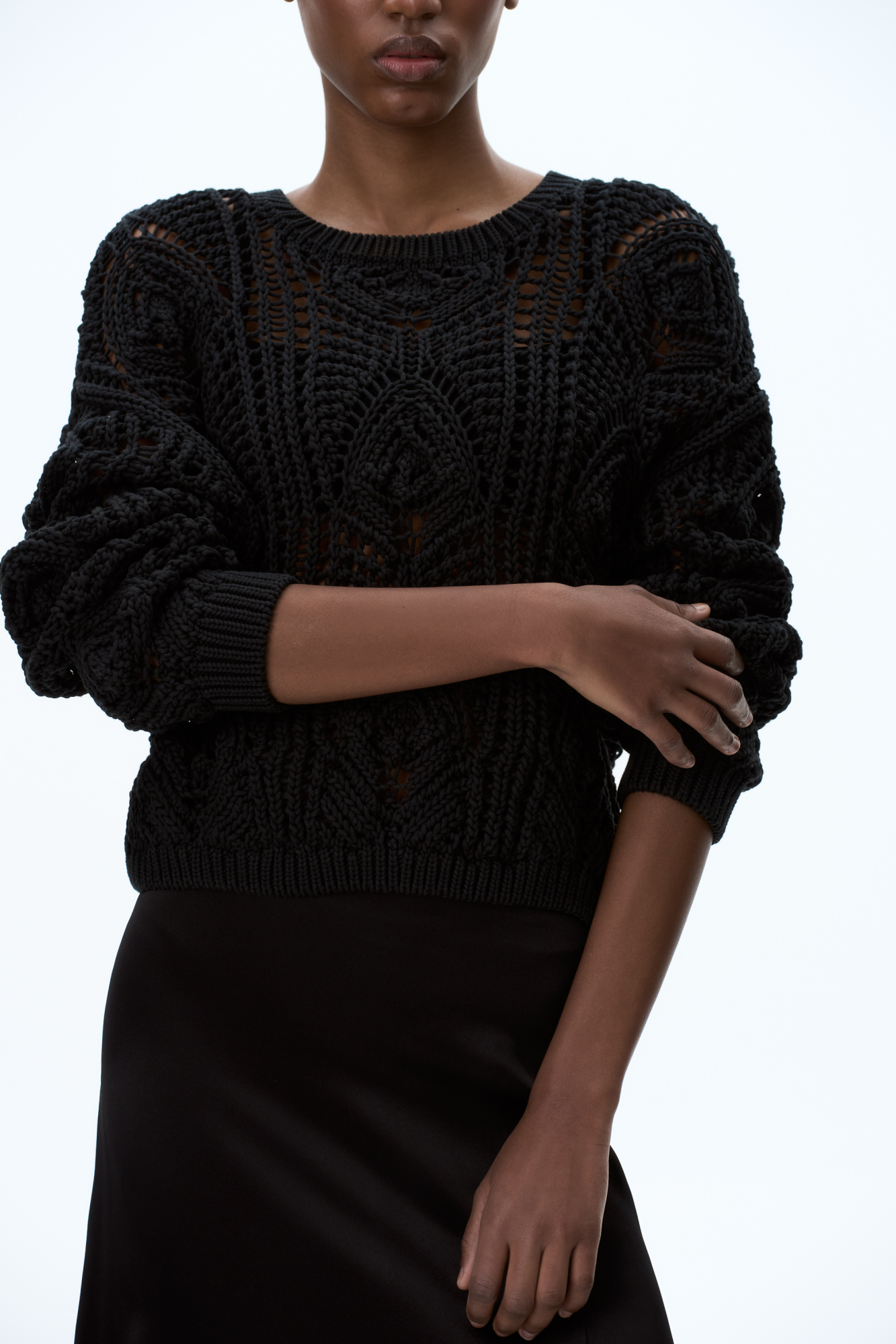 Трикотажный джемпер из хлопка, выполненный ажурной вязкой с орнаментом. Модель свободного силуэта с длинными рукавами и круглым вырезом горловины. Манжеты и низ изделия выполнены в рубчик.