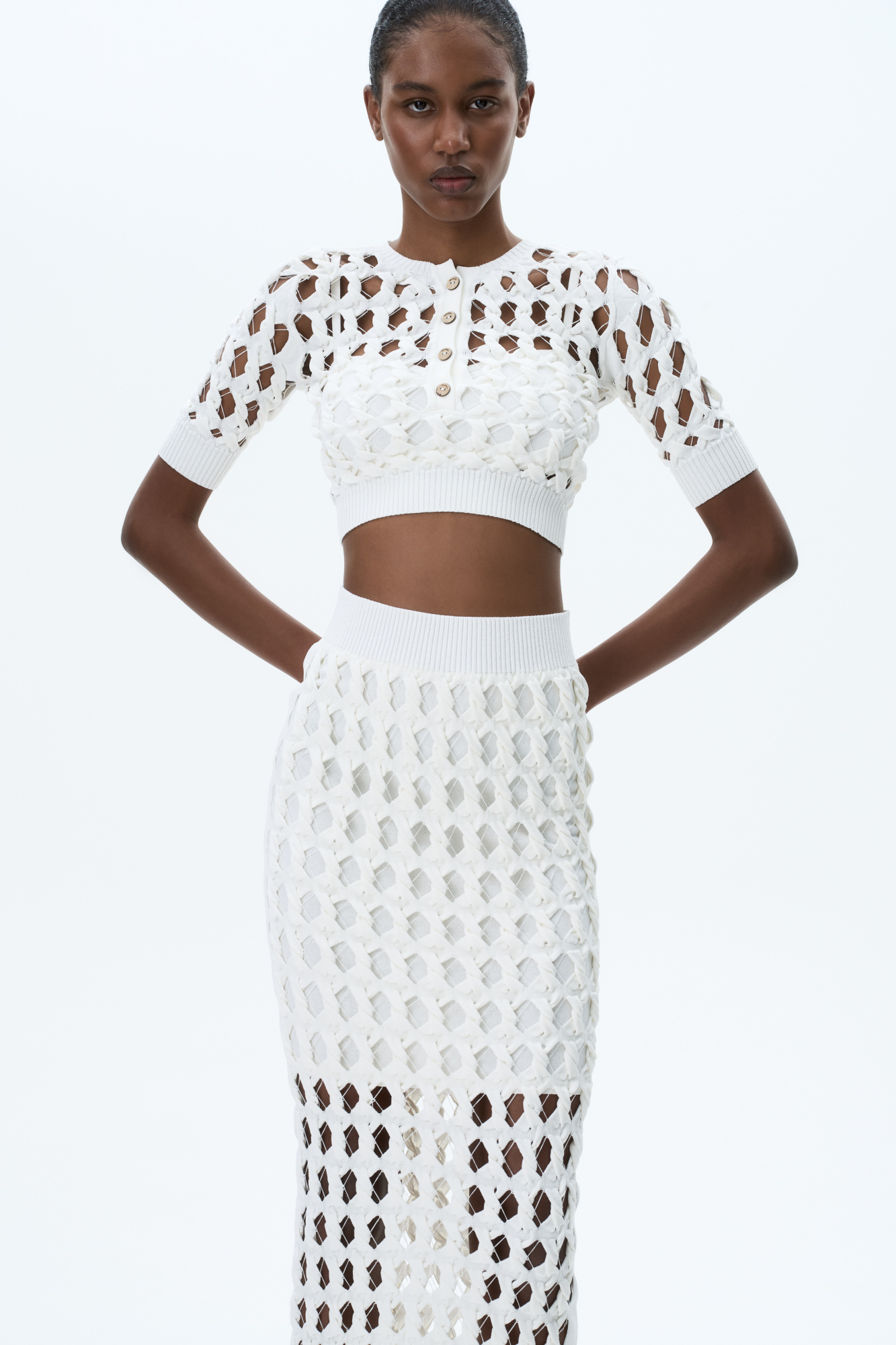 Трикотажный топ с крупным ажурным переплетением. Круглый вырез с планкой на пуговицах. На рукавах и по низу изделия широкая фактурная резинка. В комплекте топ на тонких бретелях.