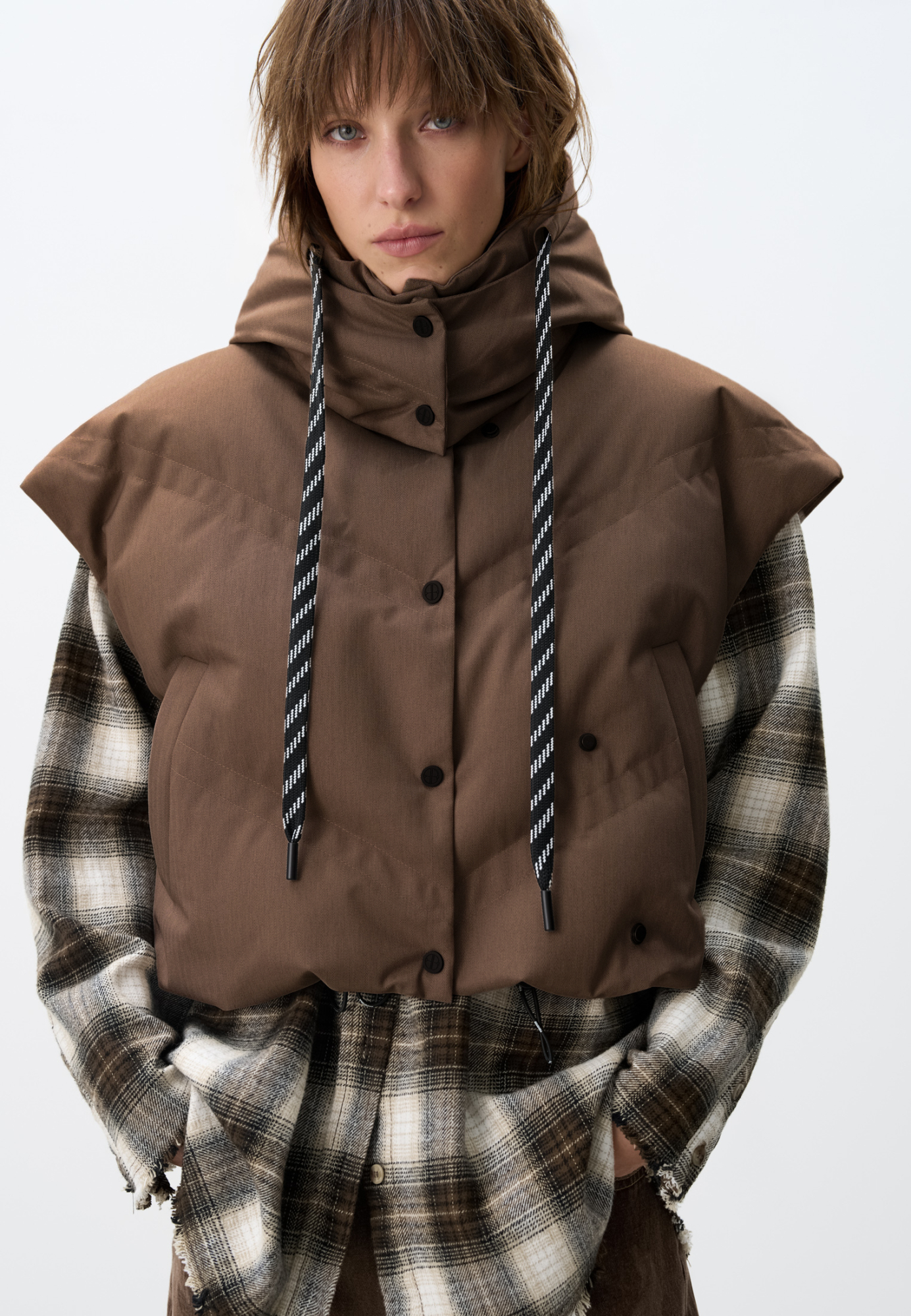 Стеганый жилет на пуху с двойной отстрочкой. Модель с капюшоном и воротником-стойкой. Застежка на кнопки. Низ изделия выполнен на регулируемой кулиске. 