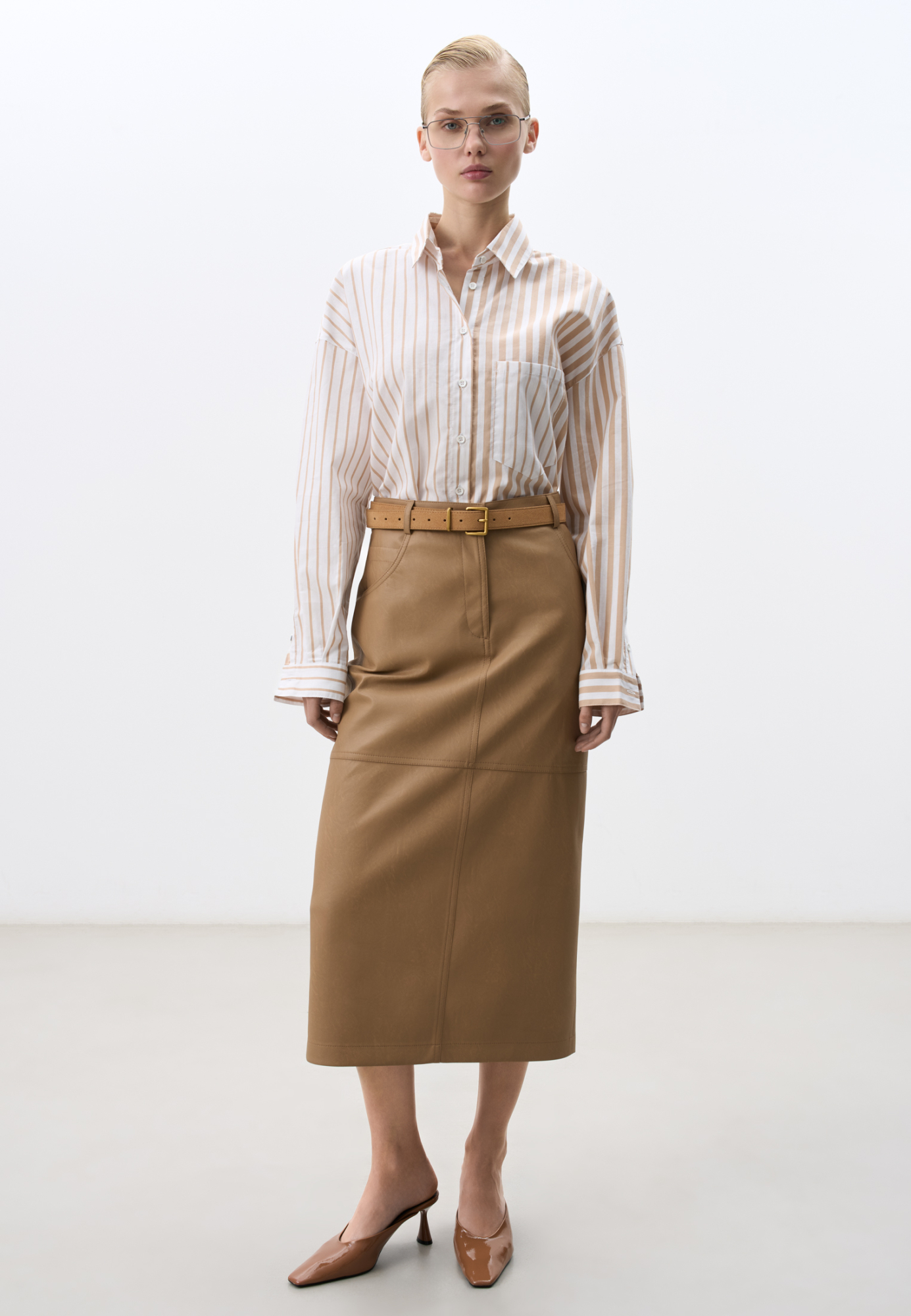 Юбка длины миди из двусторонней экокожи. Модель прямого кроя с разрезом сзади, карманами и шлевками на поясе для ремня. Застежка на пуговицу и молнию. 