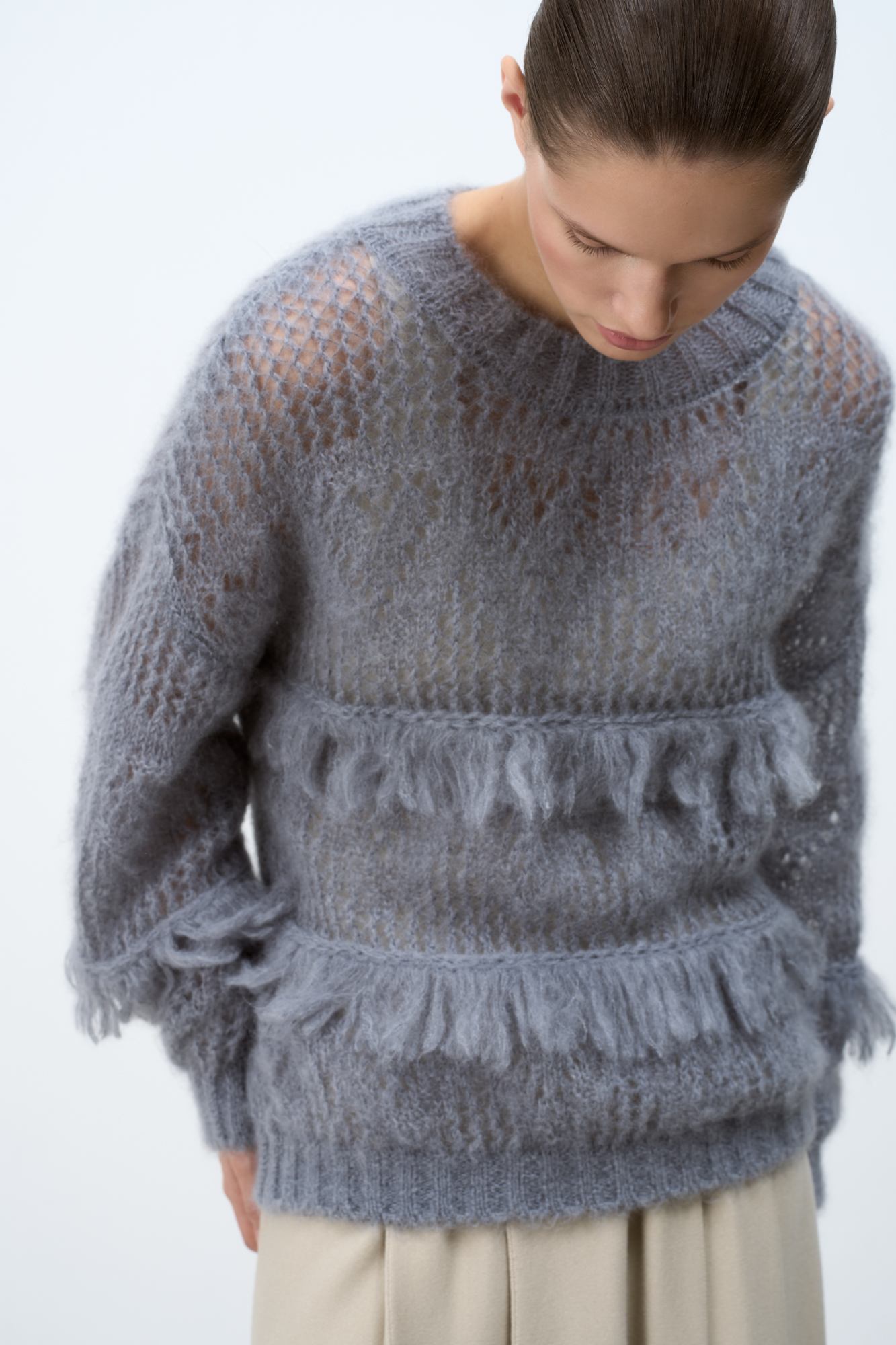 Ажурный джемпер с вывязанным узором и бахромой. Модель свободного силуэта со спущенной линией плеч и круглым вырезом горловины. Края изделия выполнены в рубчик. 