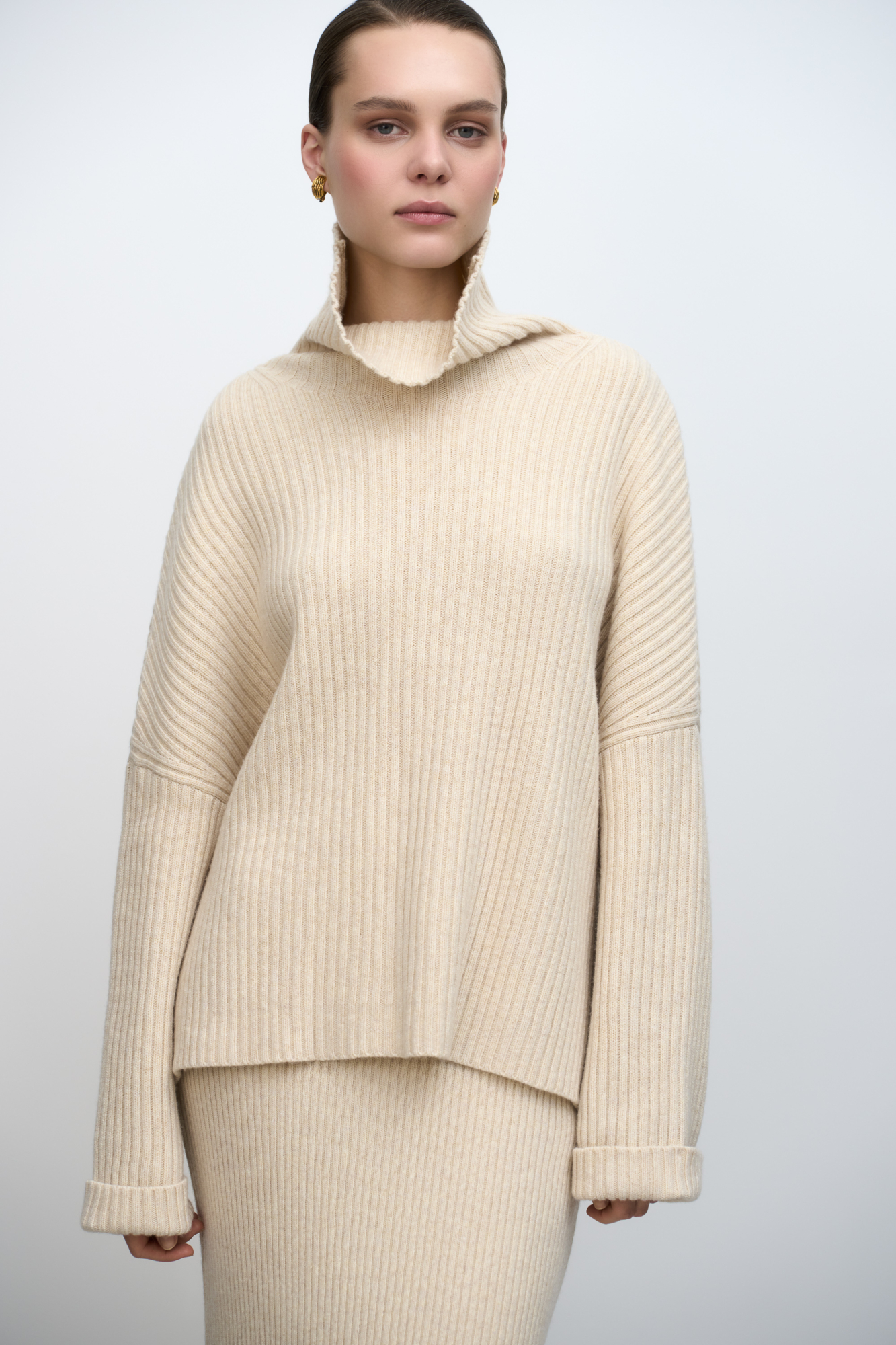 Широкий трикотажный джемпер из шерсти с добавлением кашемира. Модель свободного силуэта, со спущенной линией плеча, отворотами на манжетах и высоким свободным воротником.