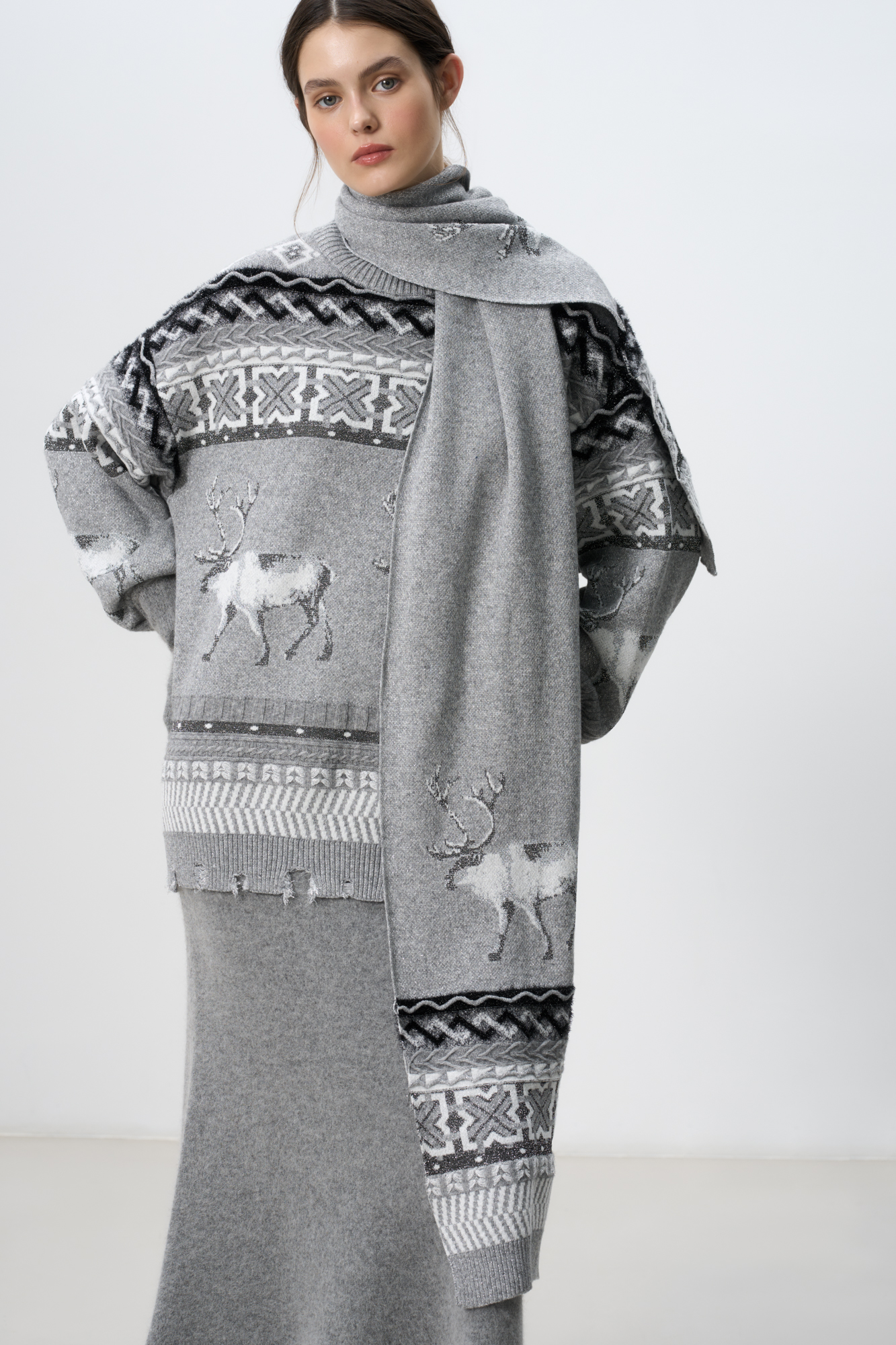 Трикотажный шарф с добавлением кашемира с жаккардовым узором в виде оленей и орнамента. Изделие декорировано люрексом. 
