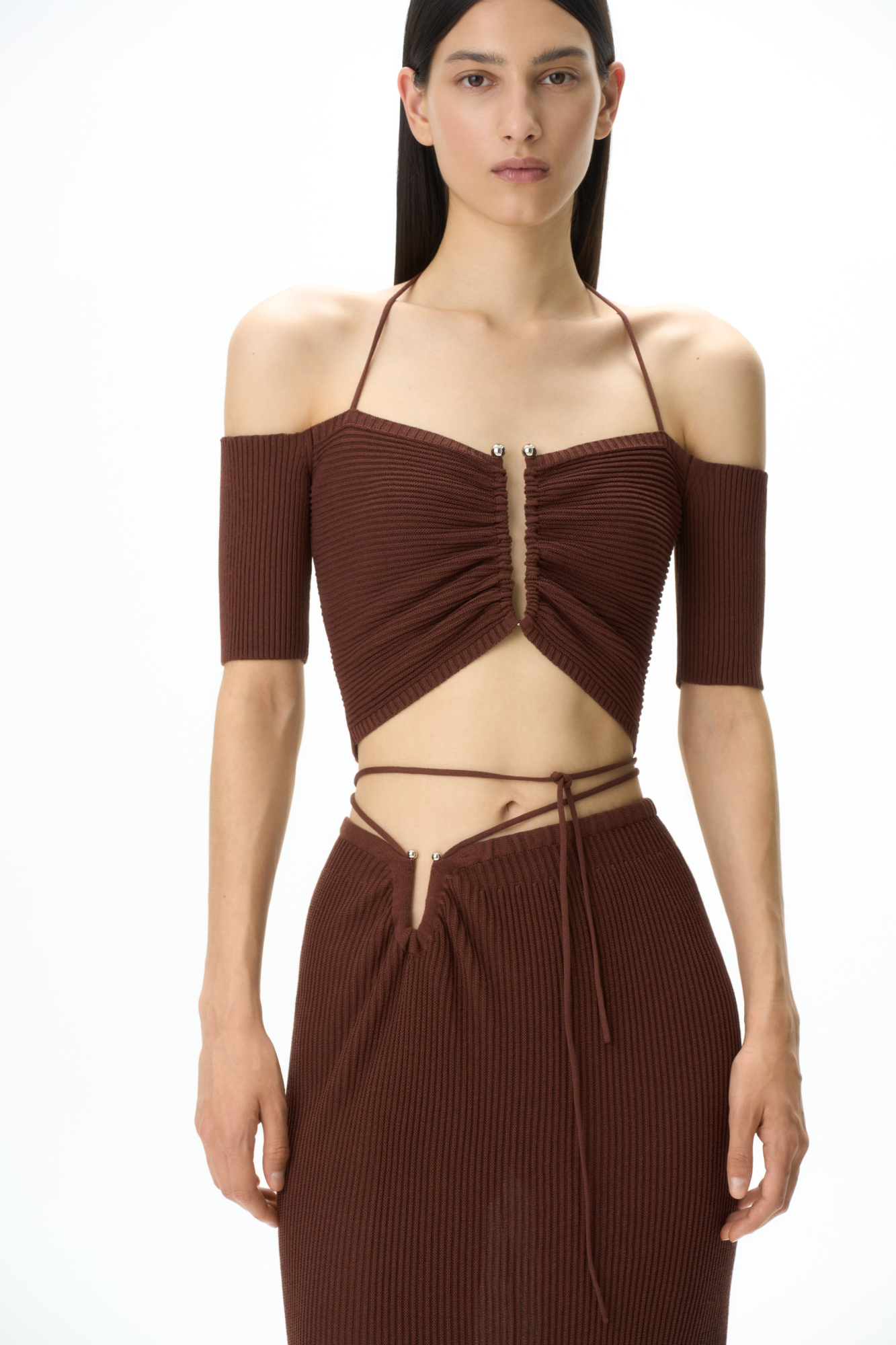 Трикотажный укороченный топ, декорированный металлической перемычкой на груди. Модель с открытыми плечами, короткими рукавами и тонкими бретелями, завязывающимися на шее.