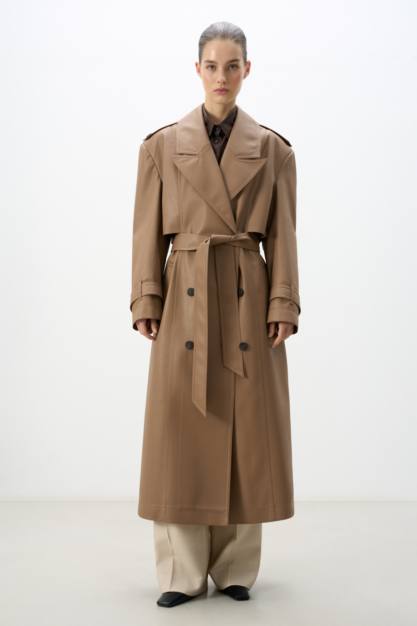 Двубортный тренч из экокожи. Модель прямого силуэта с классическим английским воротником и кокеткой. Рукава декорированы ремешками на манжетах и крупными пуговицами. Два кармана. Шлевки на талии для пояса. 
