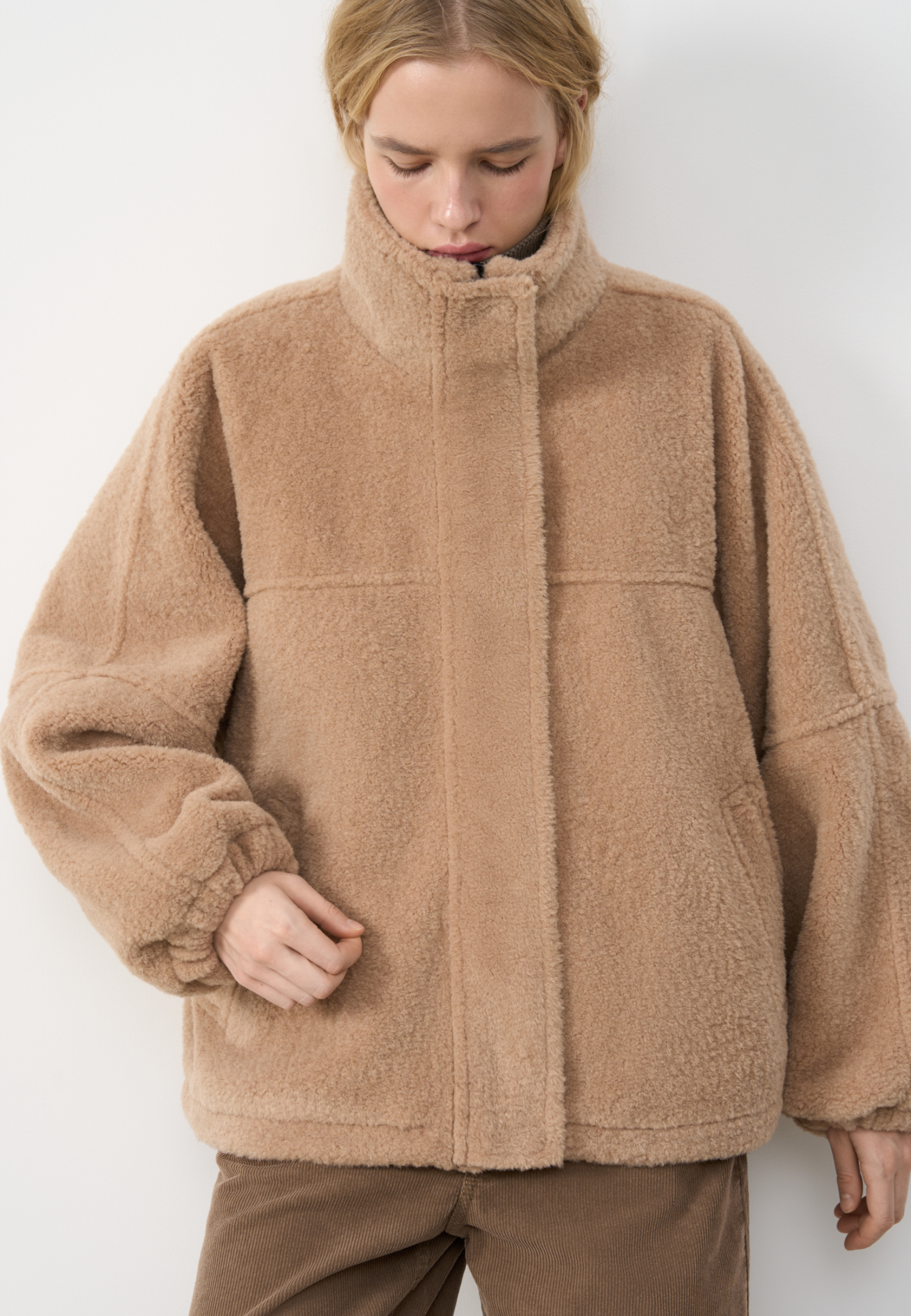 Шуба из экомеха с воротником-стойкой. Модель свободного силуэта с боковыми карманами, объемными швами и манжетами на резинке. Застежка на молнию под планкой с кнопками, декорированной экокожей.