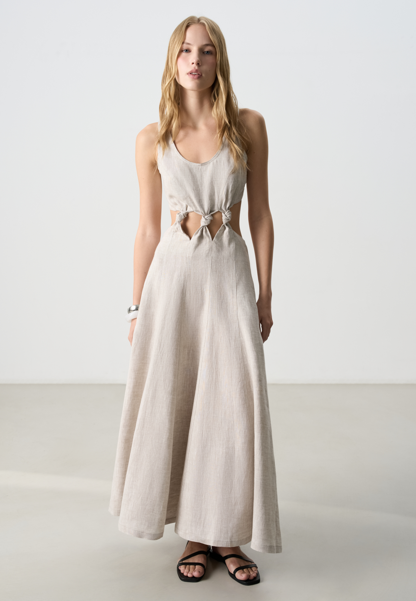 Платье длины миди из 100% льна. Модель приталенного силуэта с расклешенной юбкой, без рукавов, на широких бретельках и&nbsp;&nbsp;U-вырезом горловины. Изделие декорировано вертикальными швами и объемными узлами на талии. 
