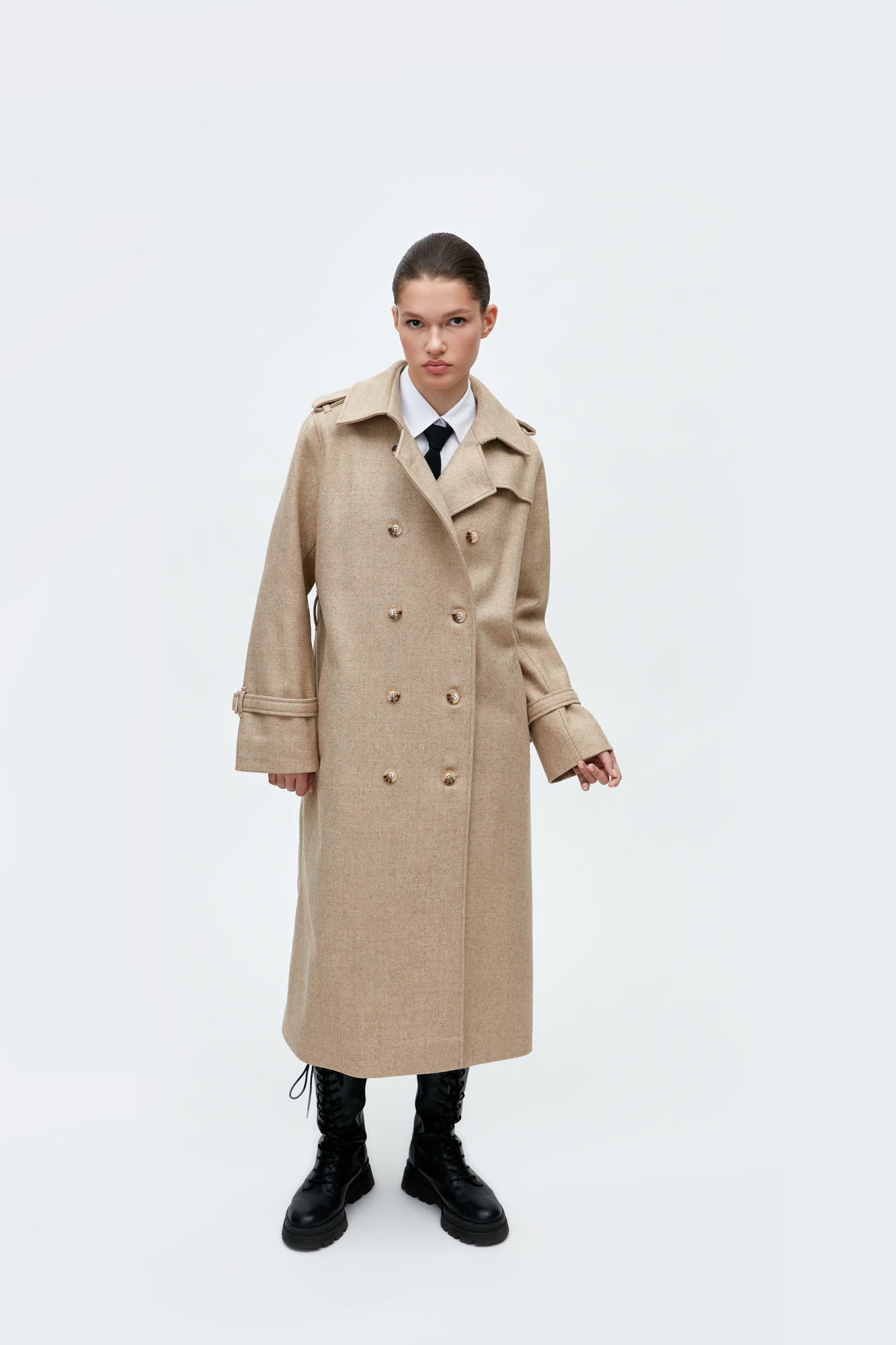 Двубортное шерстяное пальто на пуговицах приталенного силуэта, фиксированного поясом из основной ткани с пряжкой. Воротник-стойка. На плечах эполеты, рукава длинные с хлястиками. Два кармана по бокам с листочками.<br />
