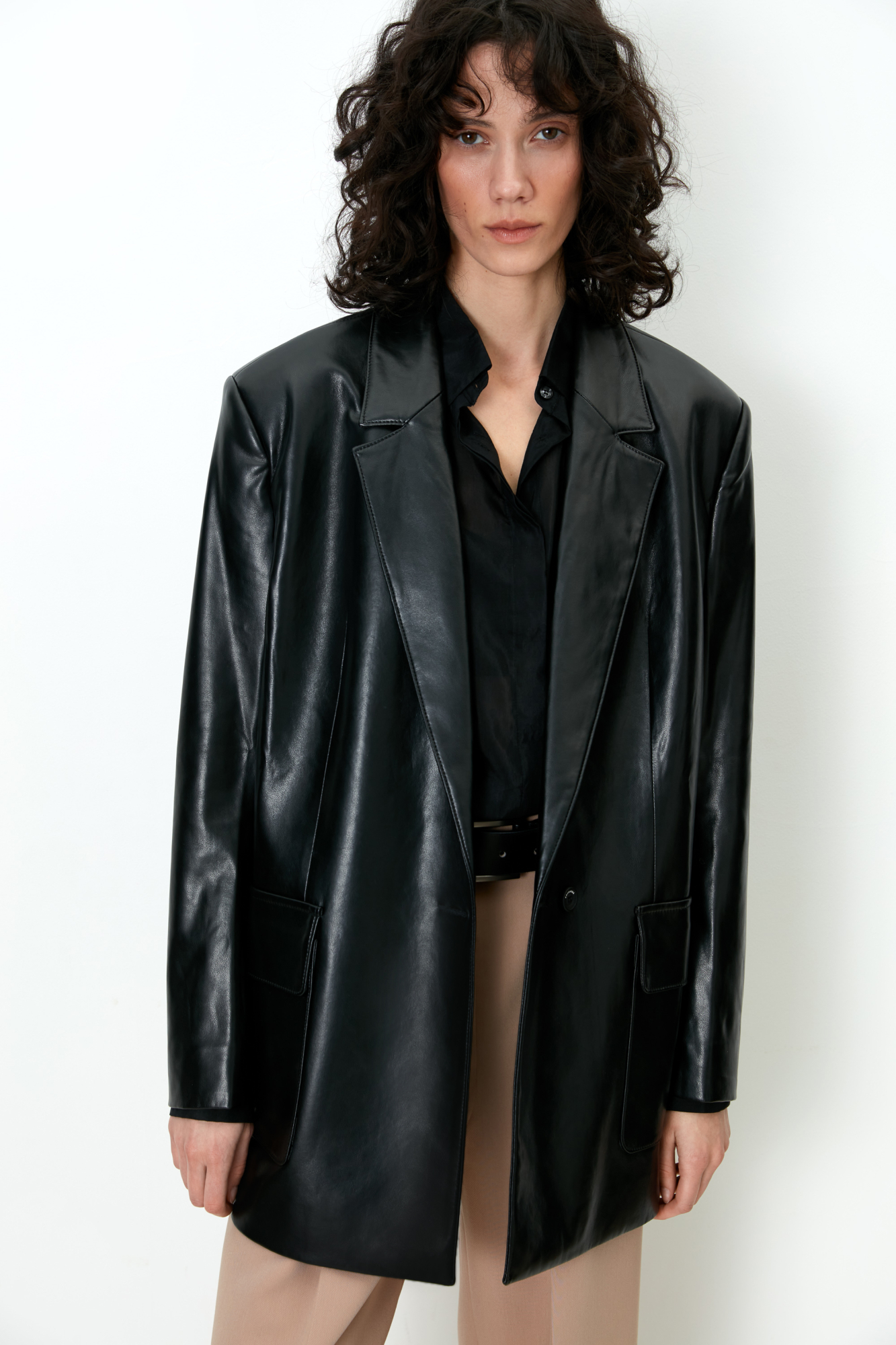 Удлиненный жакет из экокожи свободного кроя с прямоугольными лацканами. Застежка на пуговицу. Два боковых кармана с клапанами. <br />