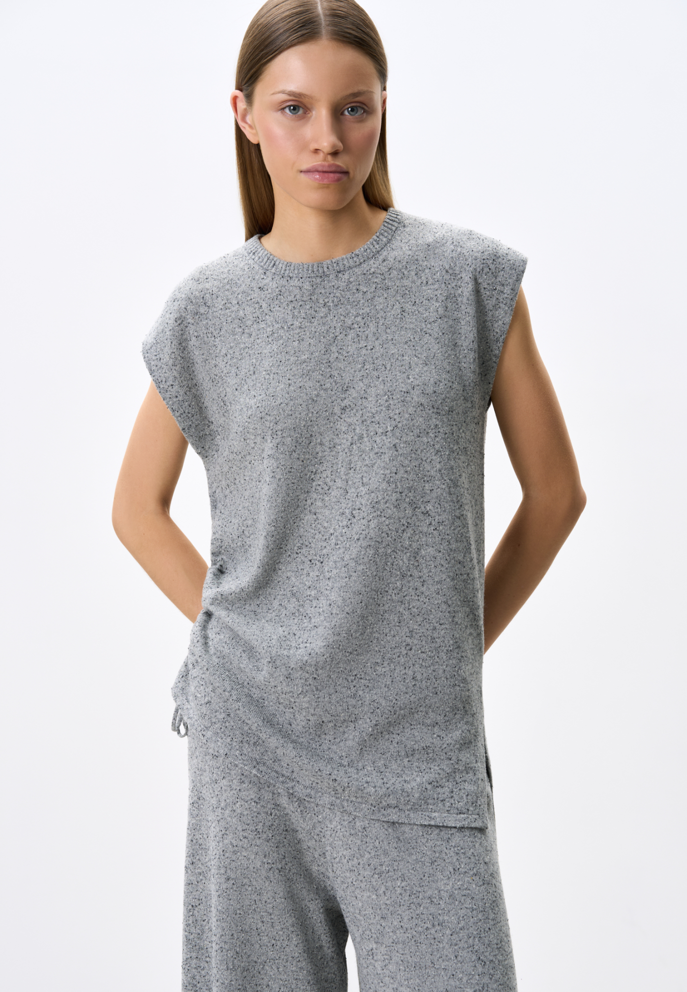 Трикотажный меланжевый жилет из мягкой шерсти с добавлением шелка и вискозы. Модель прямого силуэта без рукавов, круглый вырез, кулиска и разрез сбоку. Можно дополнить брюками из такой же пряжи.