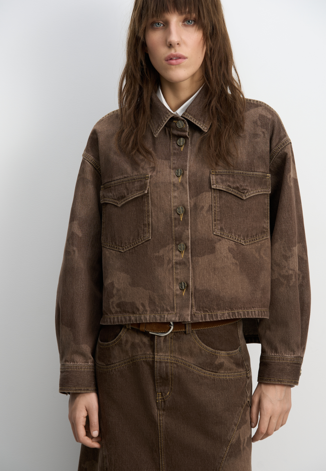 Джинсовая рубашка из 100% хлопка с принтом лошадей. Модель укороченного силуэта&nbsp;&nbsp;с длинными рукавами, классическим отложным воротником, нагрудными карманами с клапанами и застежкой на металлические пуговицы с логотипом бренда. Изделие декорировано принтом лошадей, выполненным лазером, и объемными геометрическими вытачками.<br />
Модель в стиле дерби - направления в моде, которое имитирует одежду для скачек.