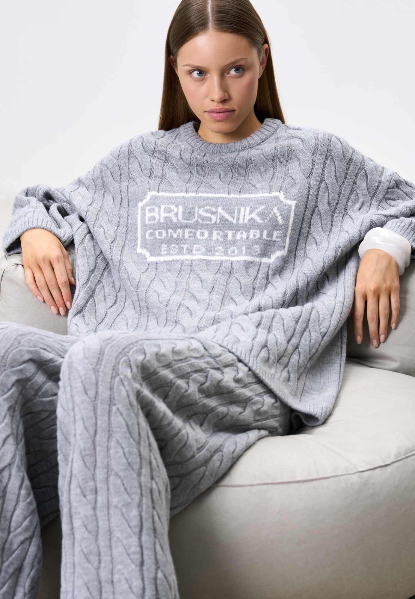 Трикотажный джемпер с объемными косами из мягкой шерсти. Модель свободного силуэта, со спущенной линией плеч и круглым вырезом. Изделие декорировано брендированным жаккардом на груди. Дополнить образ можно брюками и юбкой в том же стиле.