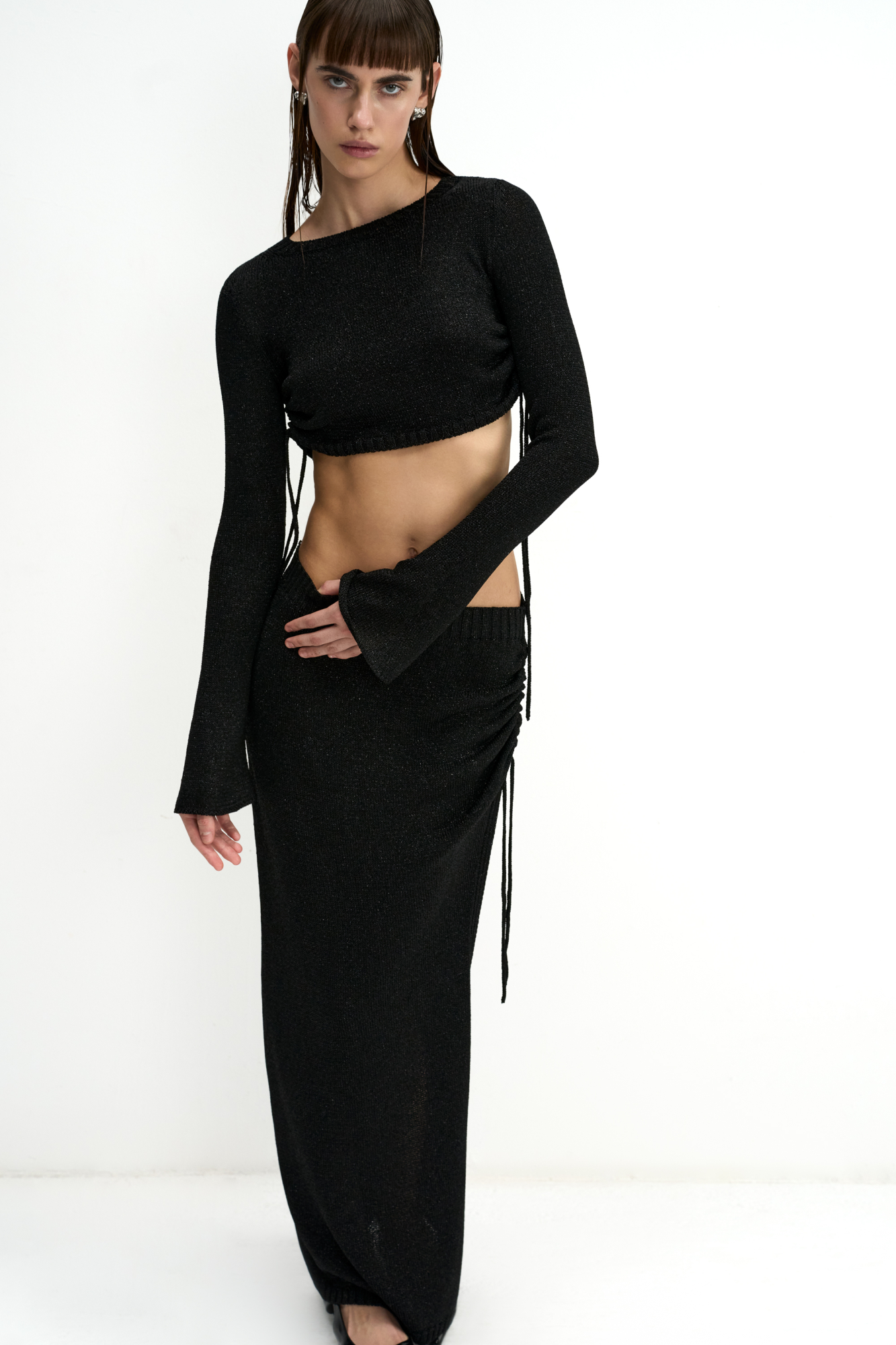 Трикотажная юбка длины макси из вискозы с люрексом. Модель облегающего силуэта, с эластичным поясом в рубчик и разрезом от бедра с кулиской. Дополнить образ можно топом в таком же стиле.