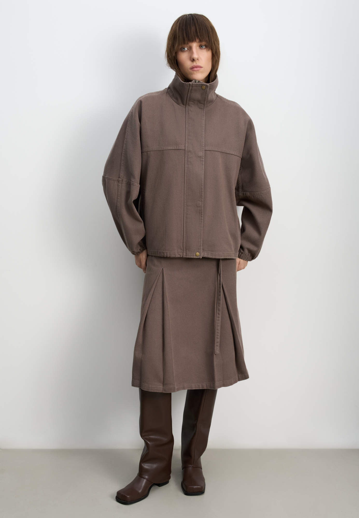 Джинсовая юбка из 100% хлопка длины миди. Модель прямого кроя, с крупными встречными складками, двойным поясом со шлевками для ремня, тонким ремешком и застежкой на молнию сбоку. 