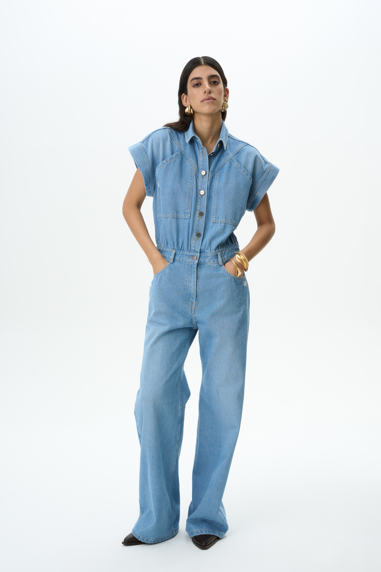 Джинсовый комбинезон из 100% хлопка. Рубашечный верх с коротким рукавом, отложным воротником и нагрудными карманами. Брюки изделия широкие, прямые, полной длины, с карманами и шлевками на поясе для ремня. Застежка на пуговицы по всей длине и молнию. Модель декорирована объемными швами и потертостями. Оттенок может отличаться от фото.